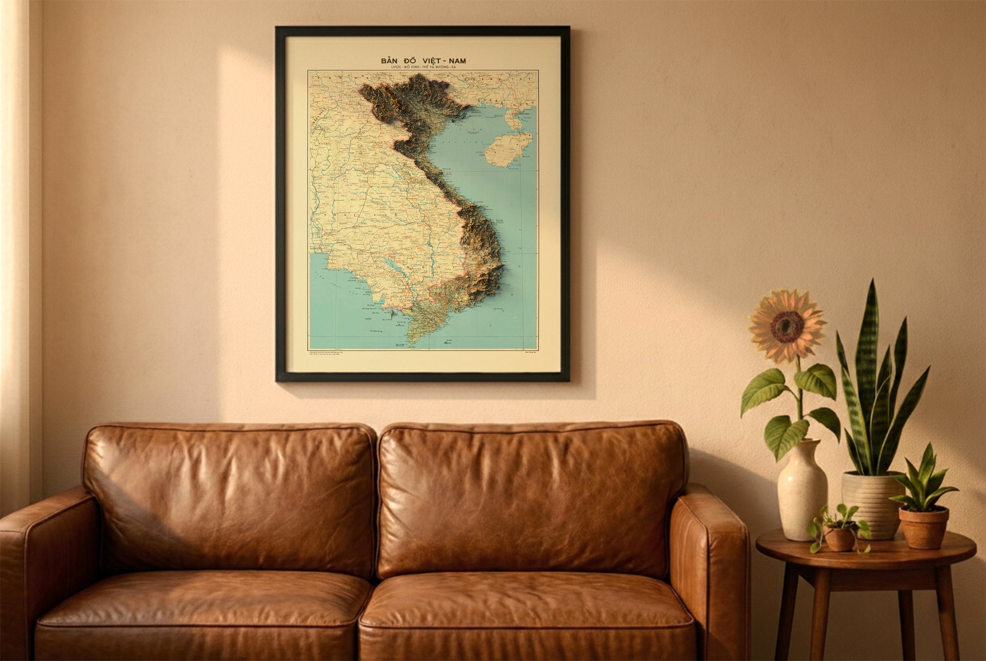 Vietnam vintage relief map in a black frame above a brown leather sofa. Boho living room with warm sunlight, sunflower, and indoor plants on a wooden side table