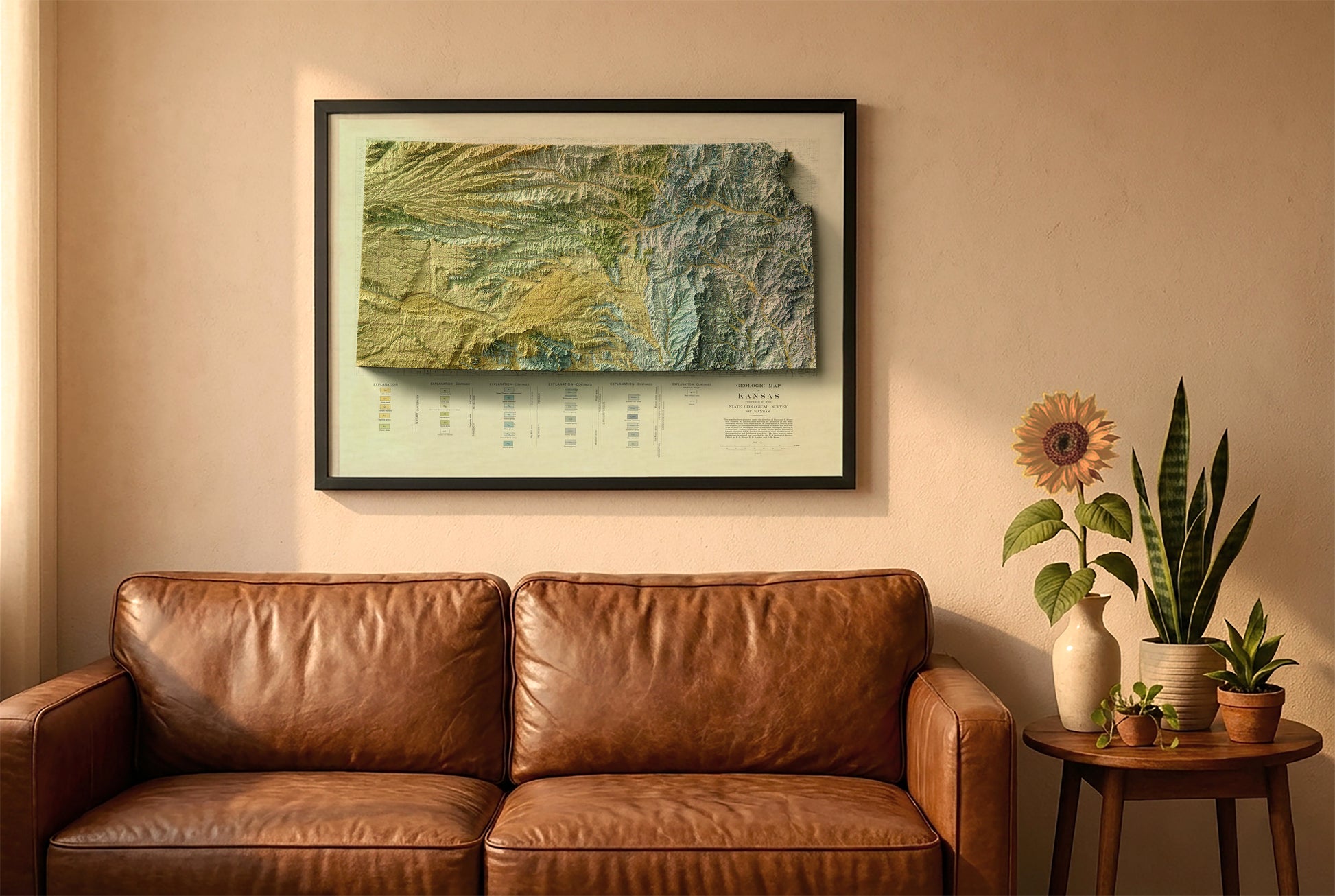 Kansas vintage relief map in a black frame above a brown leather sofa. Boho living room with warm sunlight, sunflower, and indoor plants on a wooden side table