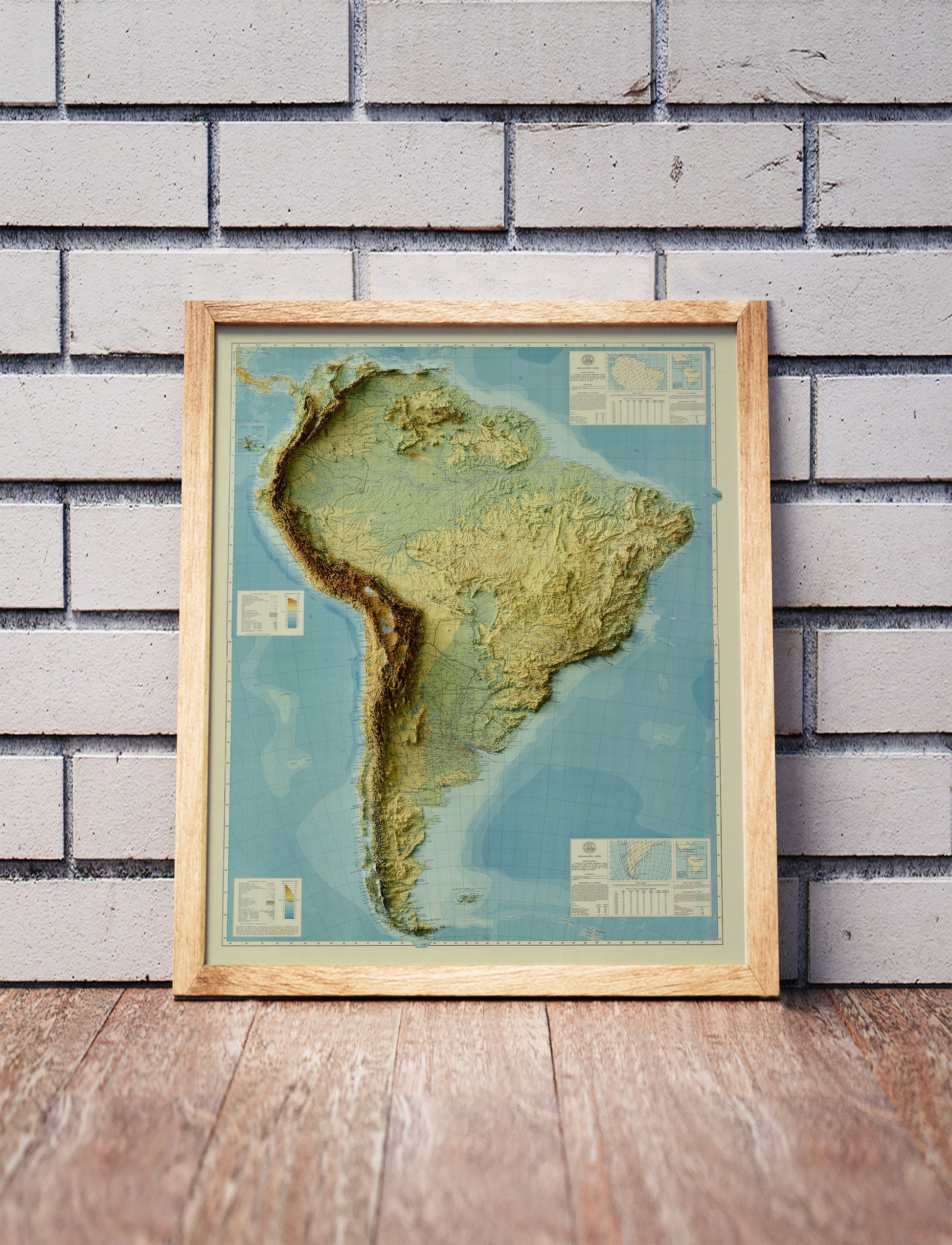 Vintage South America shaded relief map in a wooden frame. Realistic terrain art print for home decor, displayed against a brick wall