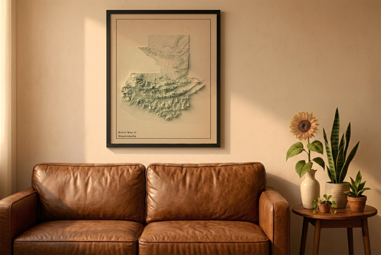 Guatemala vintage relief map in a black frame above a brown leather sofa. Boho living room with warm sunlight, sunflower, and indoor plants on a wooden side table