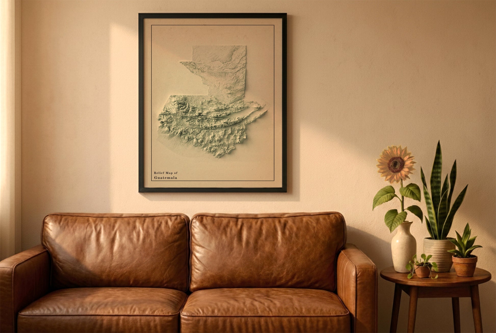 Guatemala vintage relief map in a black frame above a brown leather sofa. Boho living room with warm sunlight, sunflower, and indoor plants on a wooden side table