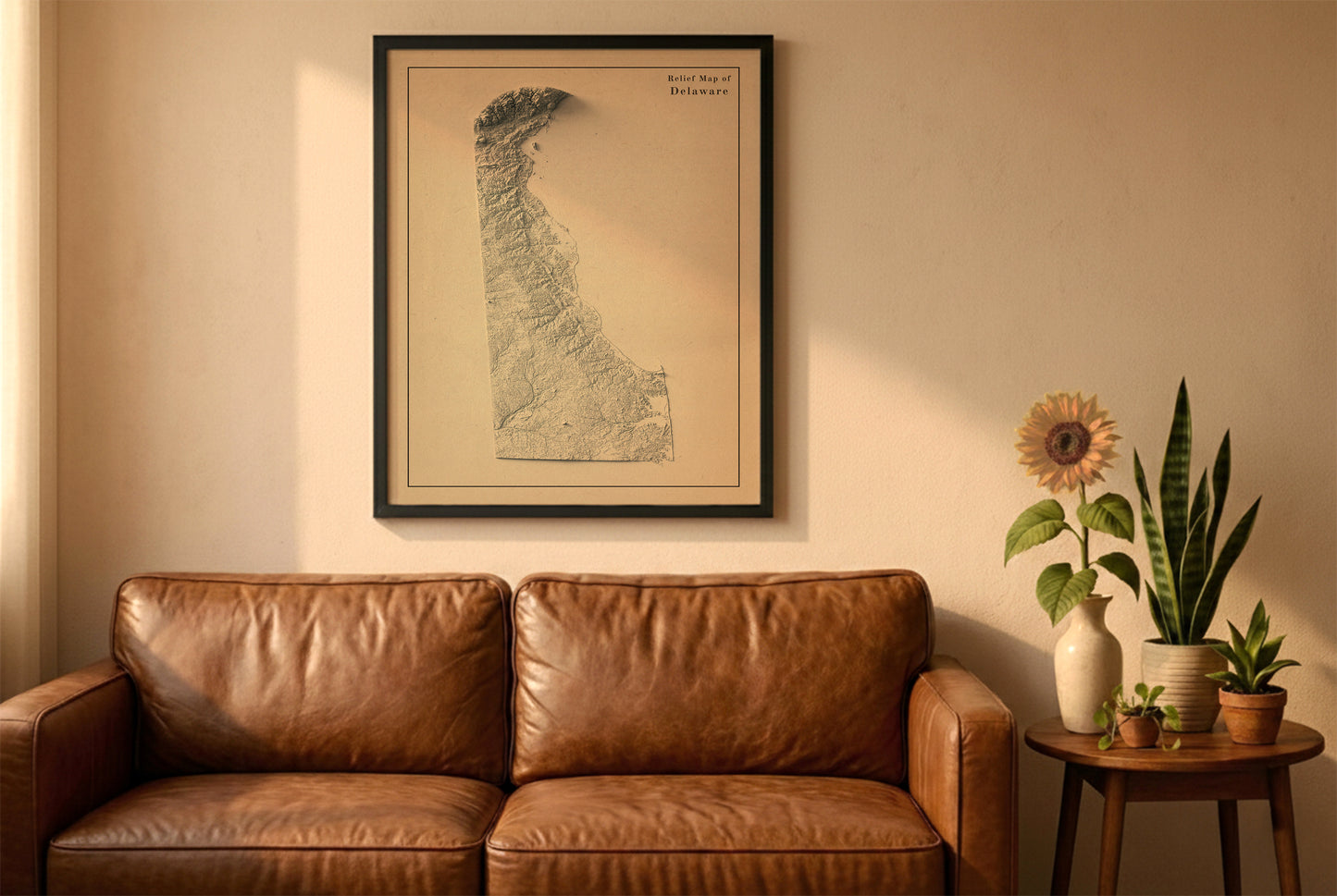 Delaware vintage relief map in a black frame above a brown leather sofa. Boho living room with warm sunlight, sunflower, and indoor plants on a wooden side table