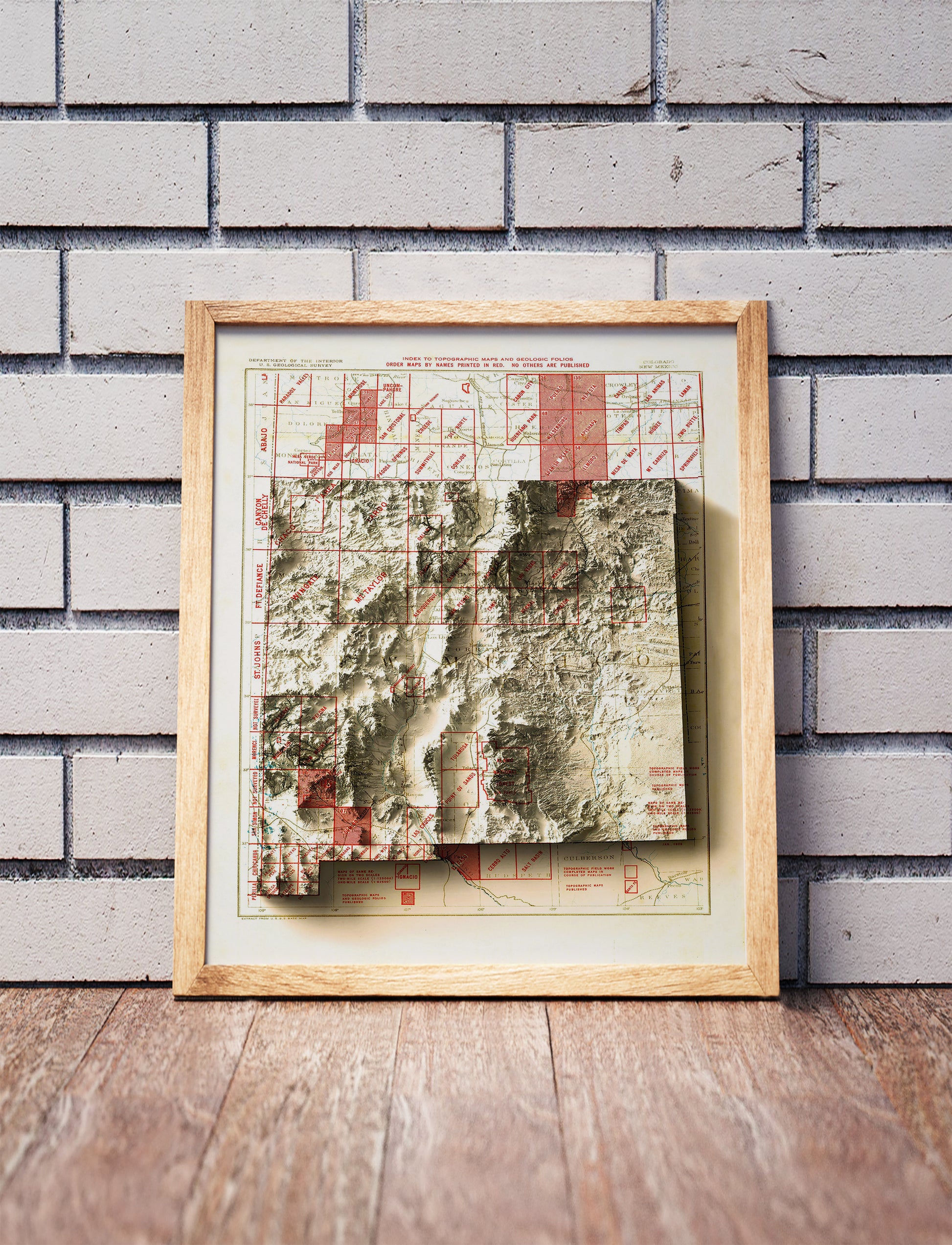 Vintage New Mexico shaded relief map in a wooden frame. Realistic terrain art print for home decor, displayed against a brick wall