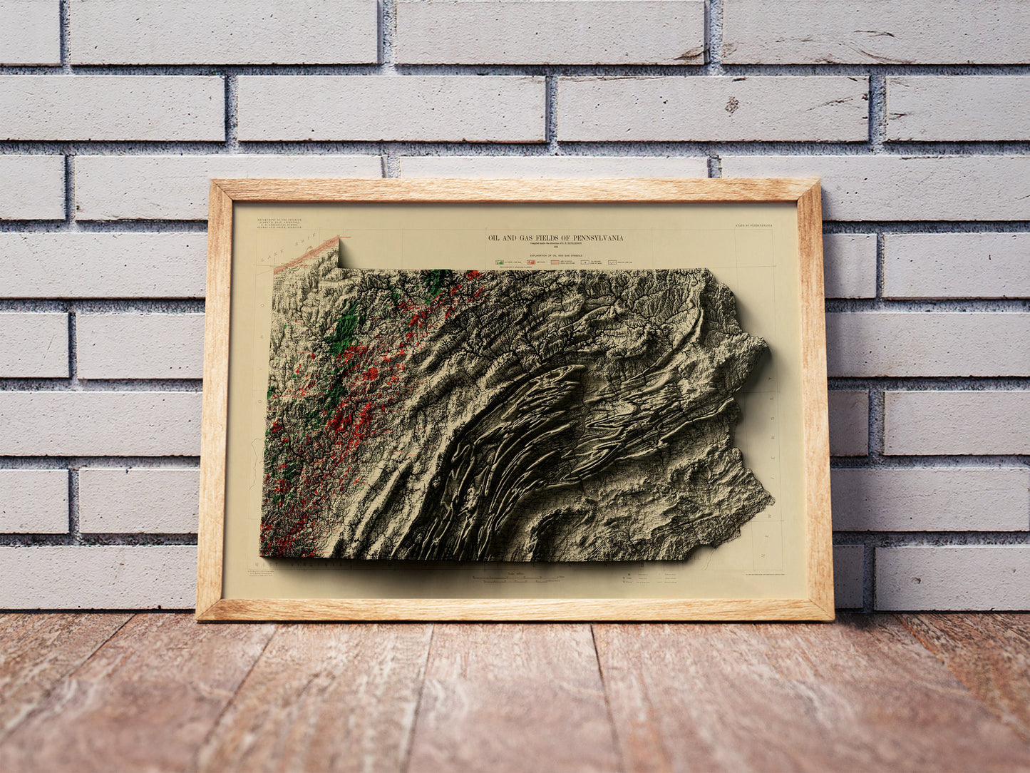 Vintage Pennsylvania shaded relief map in a wooden frame. Realistic terrain art print for home decor, displayed against a brick wall