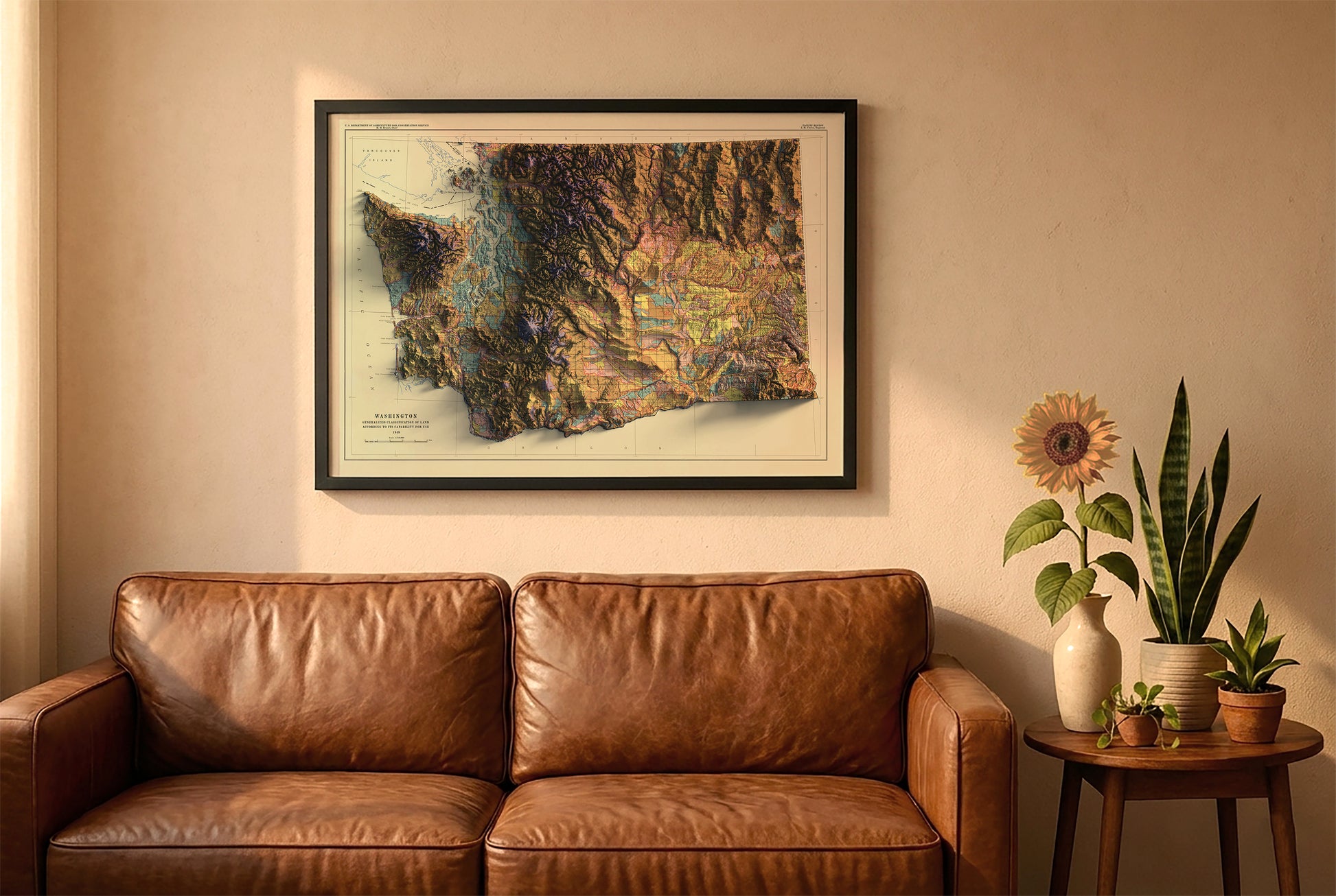 Washington vintage relief map in a black frame above a brown leather sofa. Boho living room with warm sunlight, sunflower, and indoor plants on a wooden side table