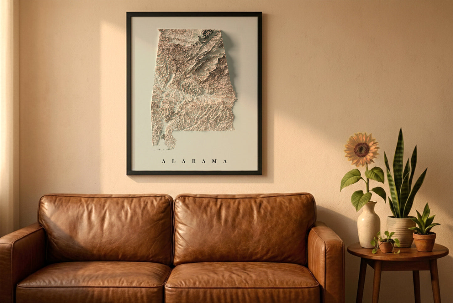 Alabama relief map in a black frame above a brown leather sofa. Boho living room with warm sunlight, sunflower, and indoor plants on a wooden side table