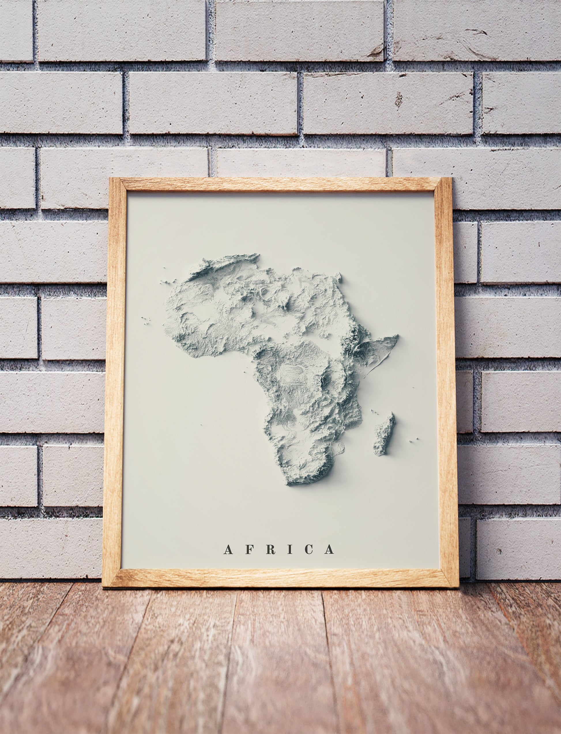 Africa shaded relief map in a wooden frame. Realistic terrain art print for home decor, displayed against a brick wall