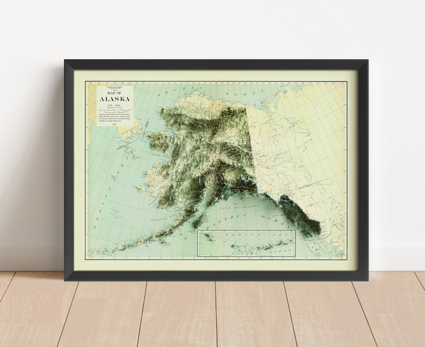 Alaska vintage relief map in a black frame above a brown leather sofa. Boho living room with warm sunlight, sunflower, and indoor plants on a wooden side table