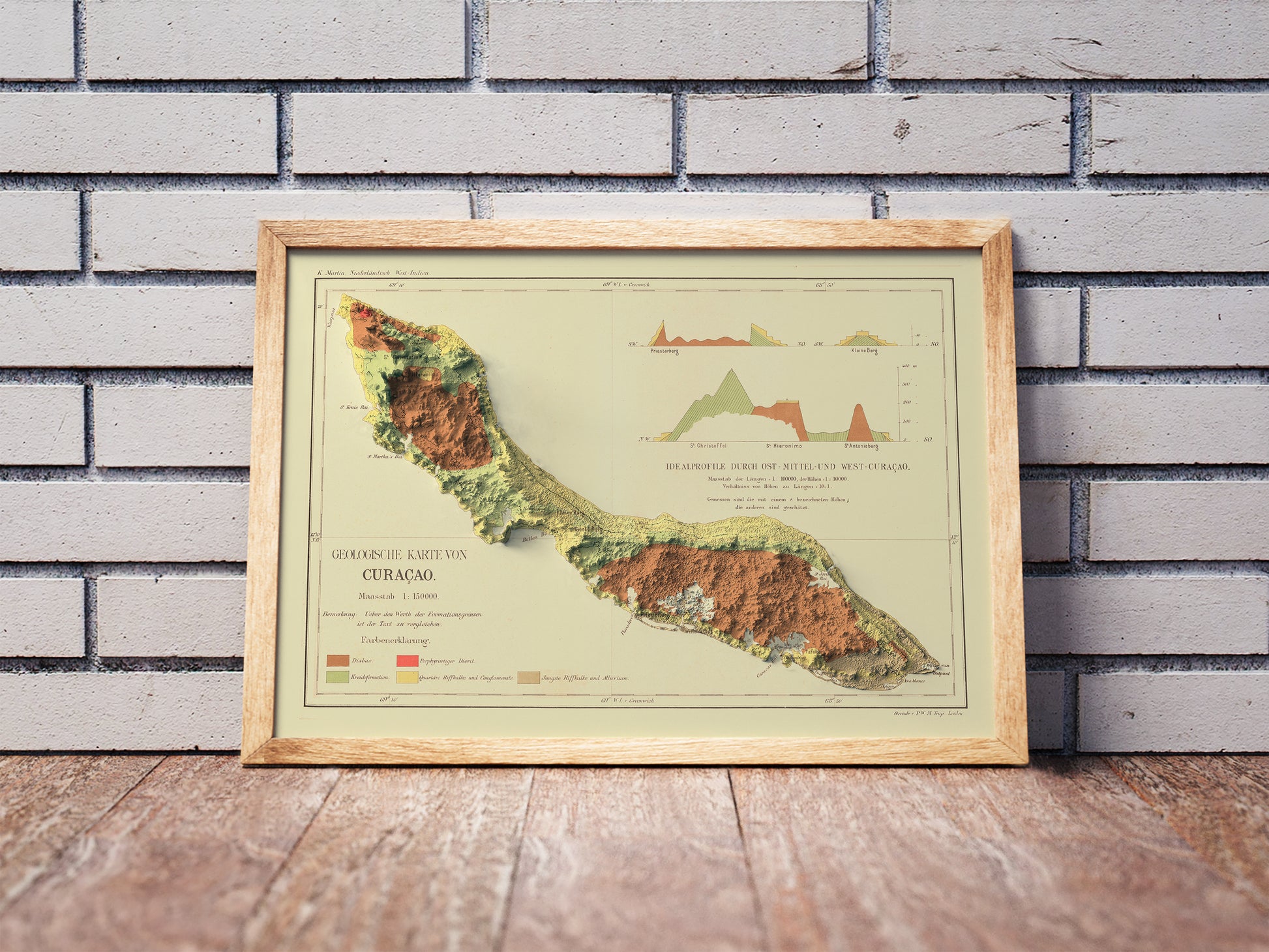 Vintage Curaçao shaded relief map in a wooden frame. Realistic terrain art print for home decor, displayed against a brick wall