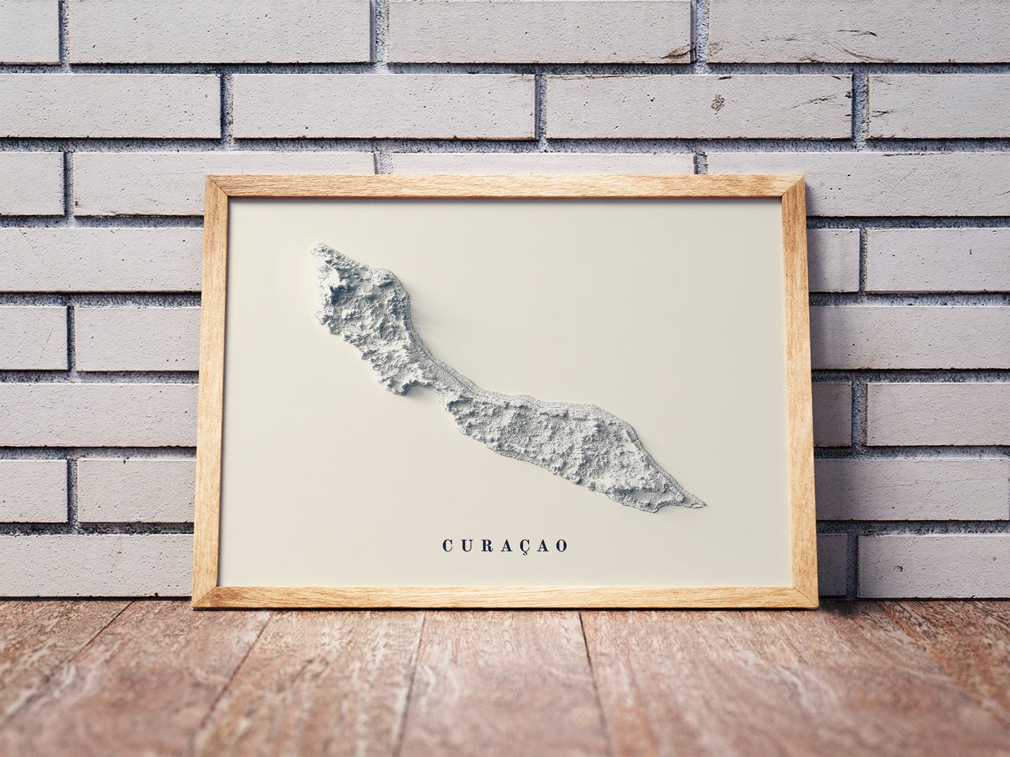 Curaçao shaded relief map in a wooden frame. Realistic terrain art print for home decor, displayed against a brick wall
