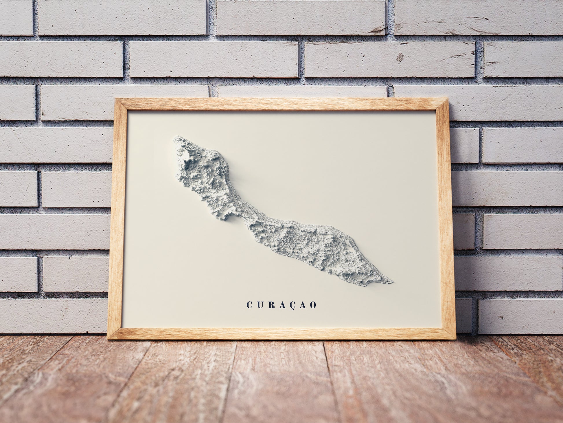 Curaçao shaded relief map in a wooden frame. Realistic terrain art print for home decor, displayed against a brick wall