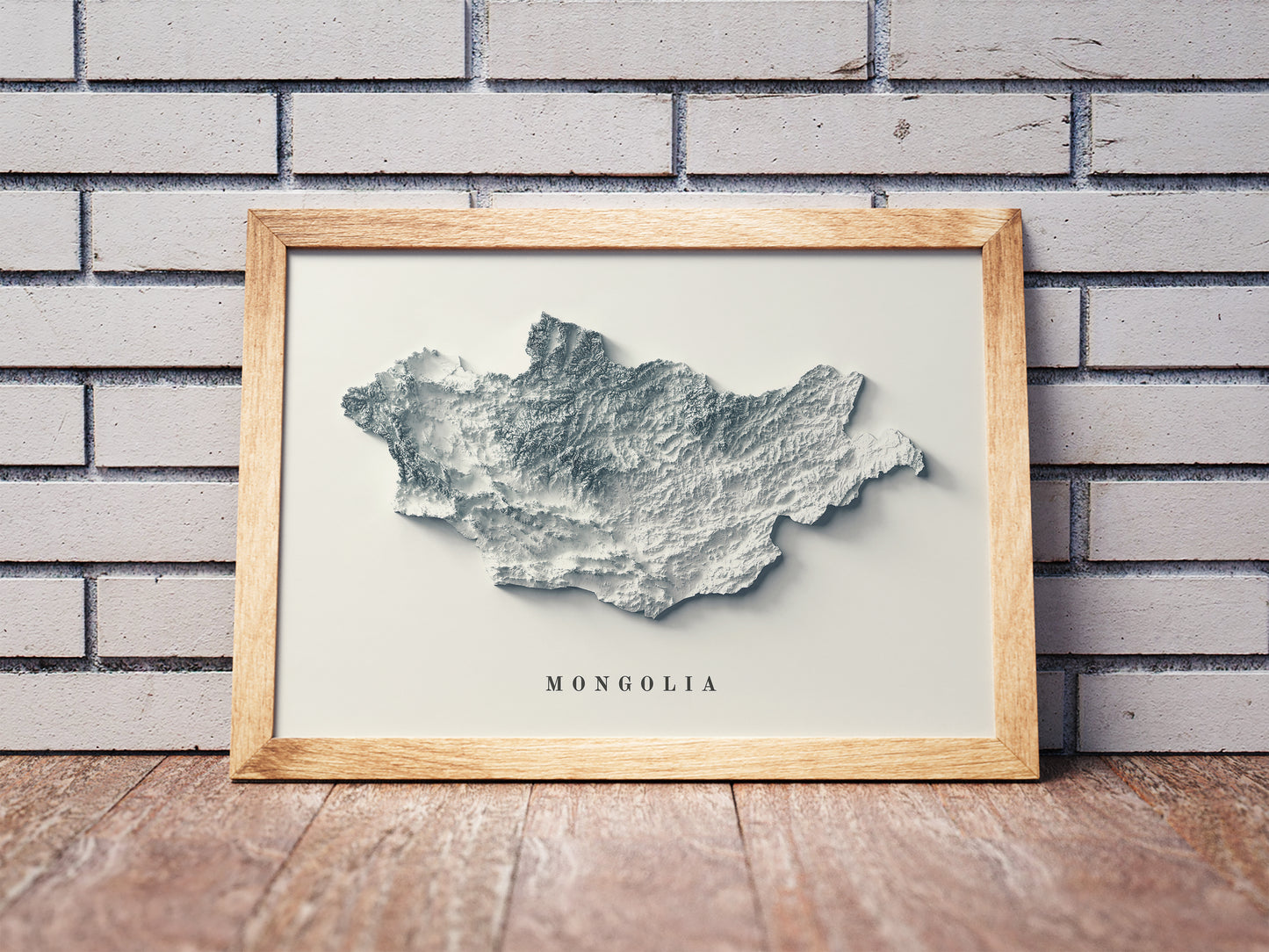 Mongolia shaded relief map in a wooden frame. Realistic terrain art print for home decor, displayed against a brick wall