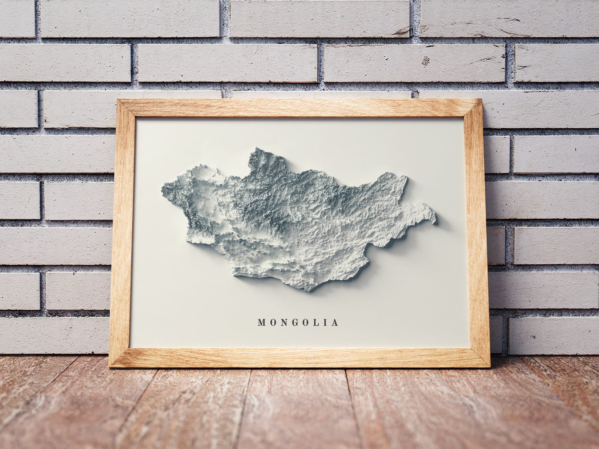 Mongolia shaded relief map in a wooden frame. Realistic terrain art print for home decor, displayed against a brick wall