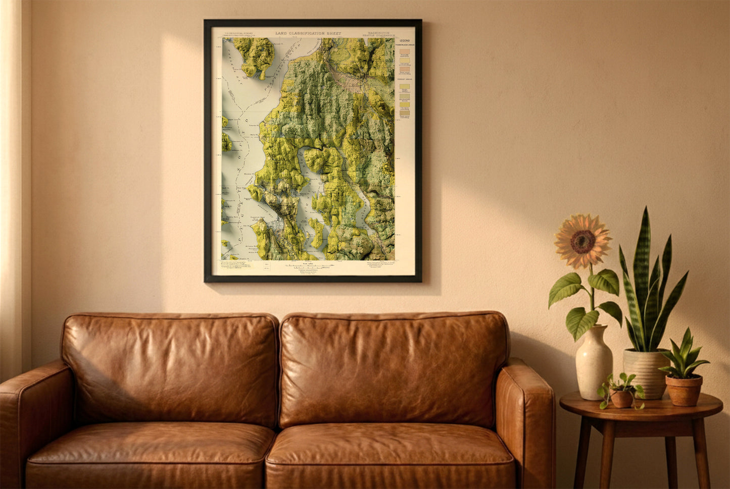 Seattle vintage relief map in a black frame above a brown leather sofa. Boho living room with warm sunlight, sunflower, and indoor plants on a wooden side table