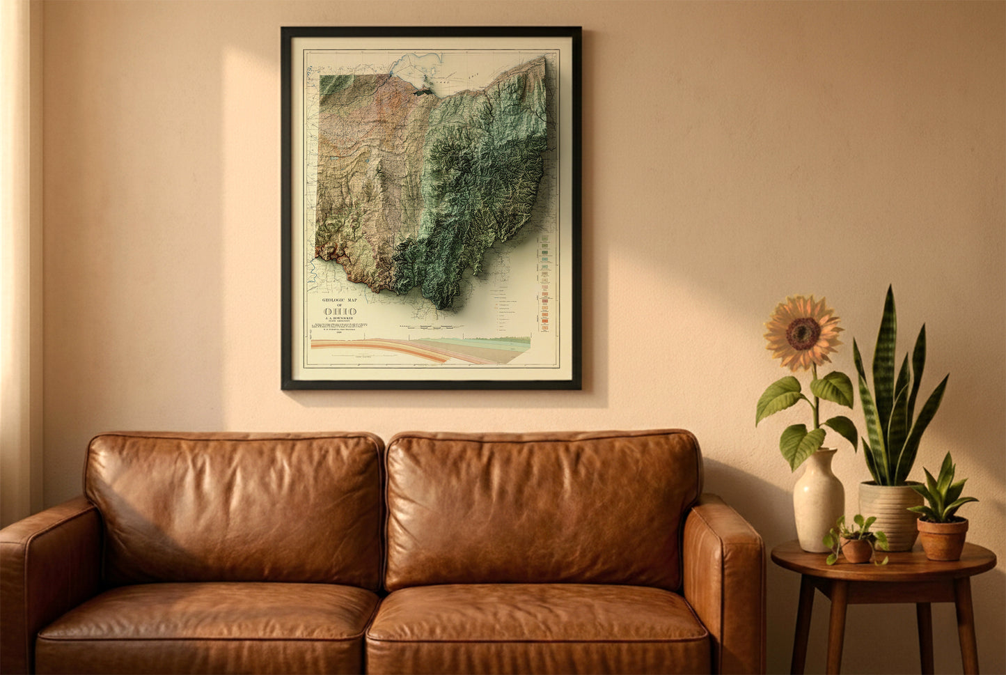Ohio vintage relief map in a black frame above a brown leather sofa. Boho living room with warm sunlight, sunflower, and indoor plants on a wooden side table