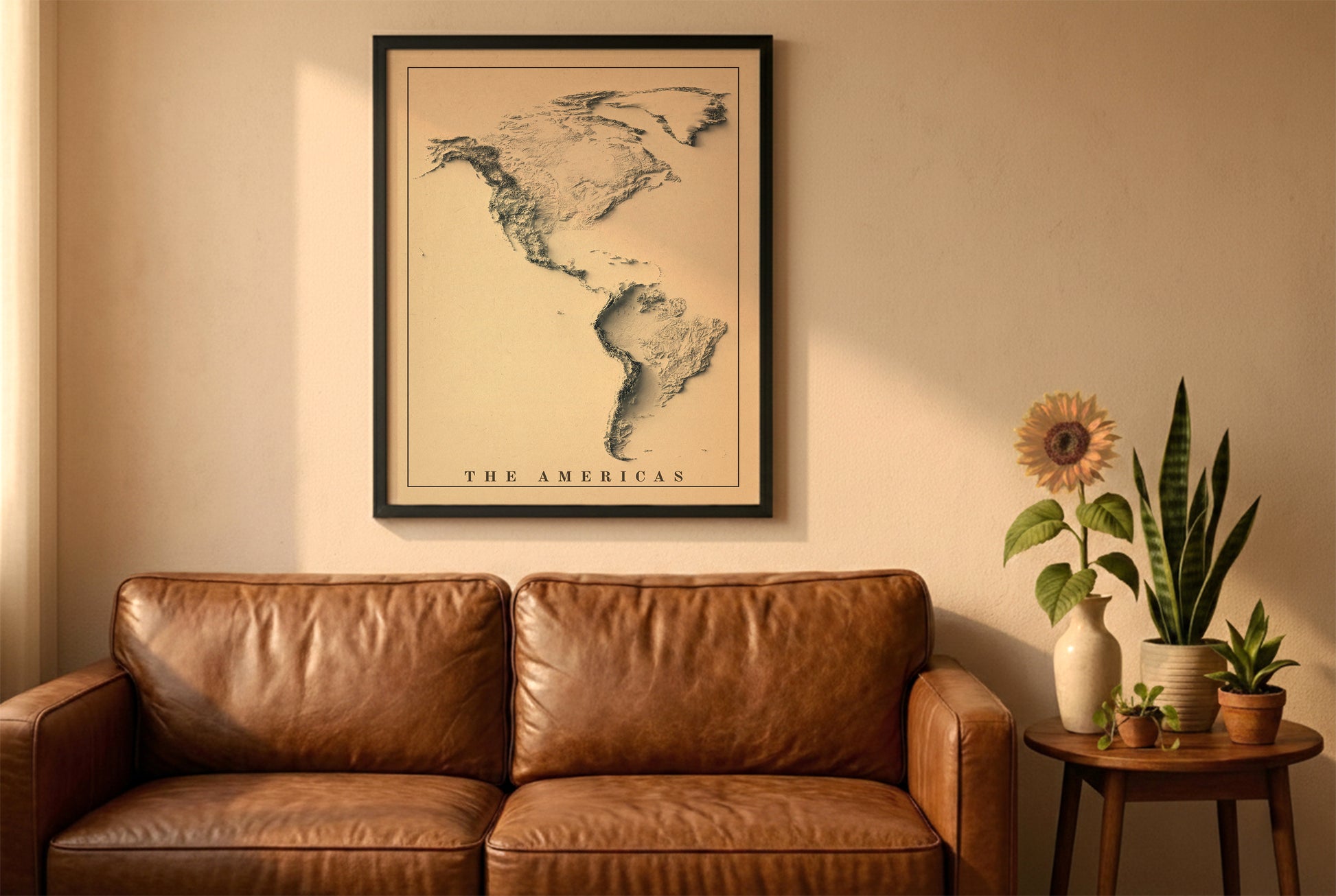 The Americas vintage relief map in a black frame above a brown leather sofa. Boho living room with warm sunlight, sunflower, and indoor plants on a wooden side table
