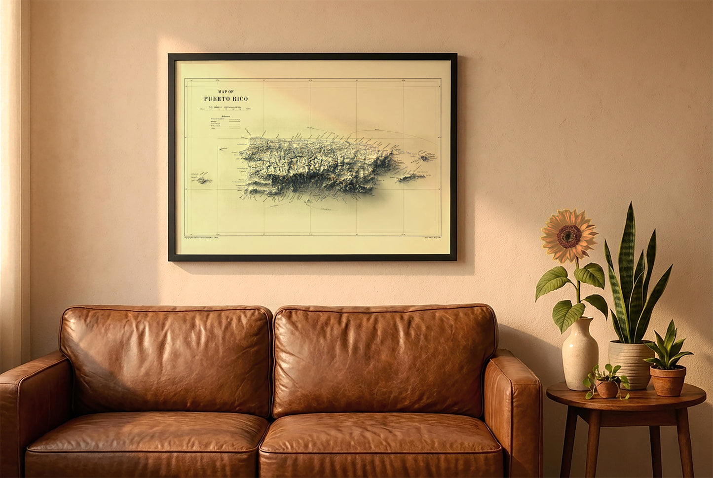 Puerto Rico vintage relief map in a black frame above a brown leather sofa. Boho living room with warm sunlight, sunflower, and indoor plants on a wooden side table