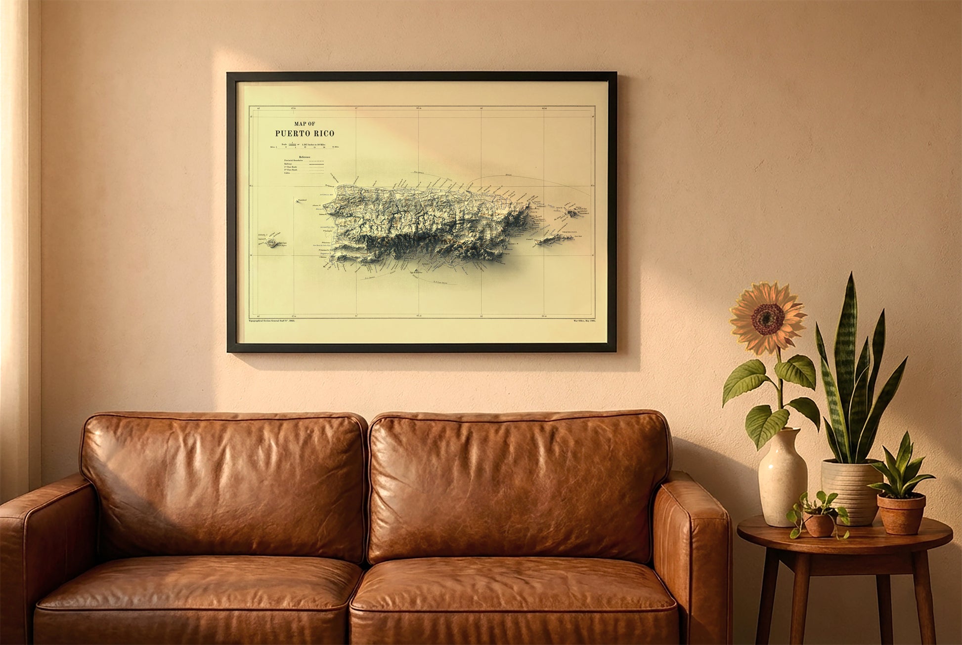 Puerto Rico vintage relief map in a black frame above a brown leather sofa. Boho living room with warm sunlight, sunflower, and indoor plants on a wooden side table