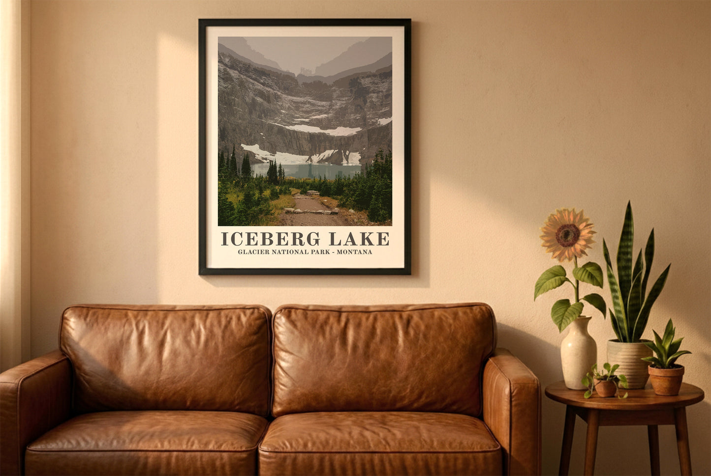 Glacier National Park poster in a black frame above a brown leather sofa. Boho living room with warm sunlight, sunflower, and indoor plants on a wooden side table