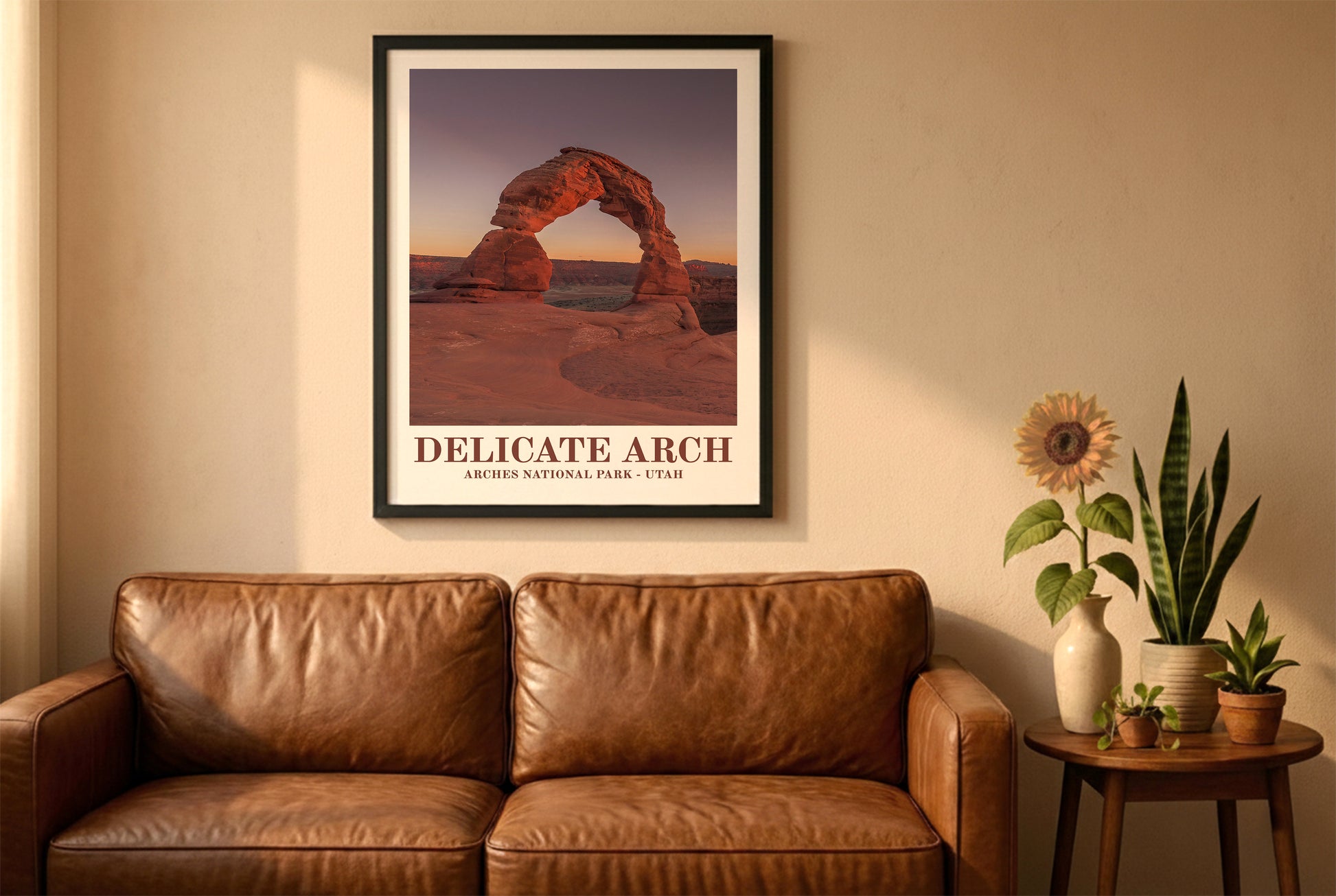 Arches National Park poster in a black frame above a brown leather sofa. Boho living room with warm sunlight, sunflower, and indoor plants on a wooden side table