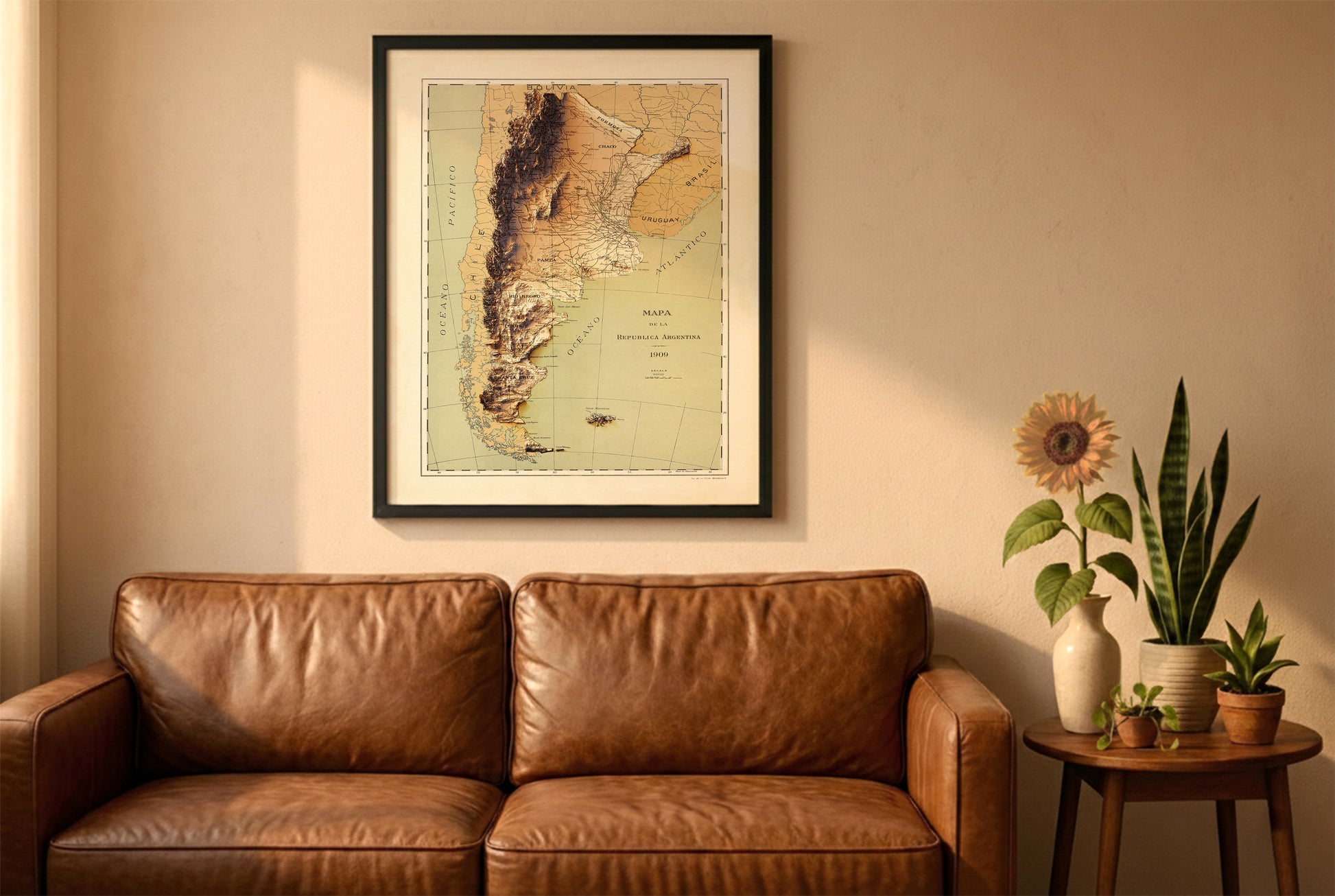 Argentina vintage relief map in a black frame above a brown leather sofa. Boho living room with warm sunlight, sunflower, and indoor plants on a wooden side table