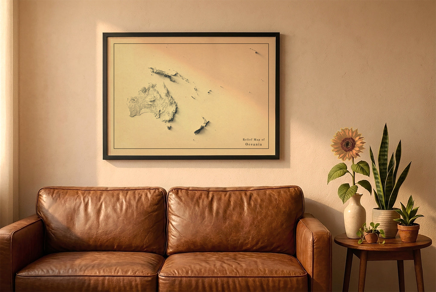 Oceania vintage relief map in a black frame above a brown leather sofa. Boho living room with warm sunlight, sunflower, and indoor plants on a wooden side table