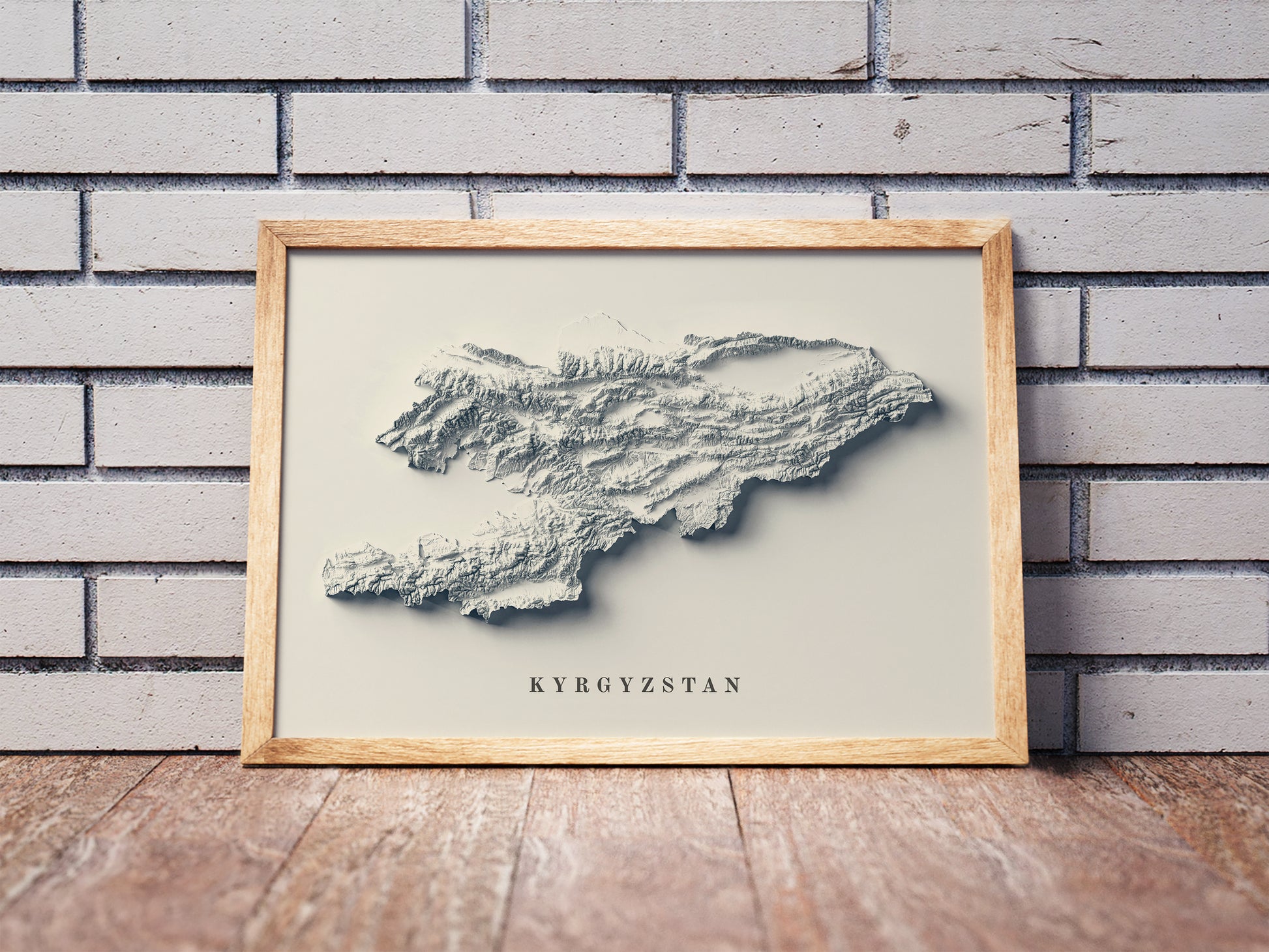 Vintage Kyrgyzstan shaded relief map in a wooden frame. Realistic terrain art print for home decor, displayed against a brick wall