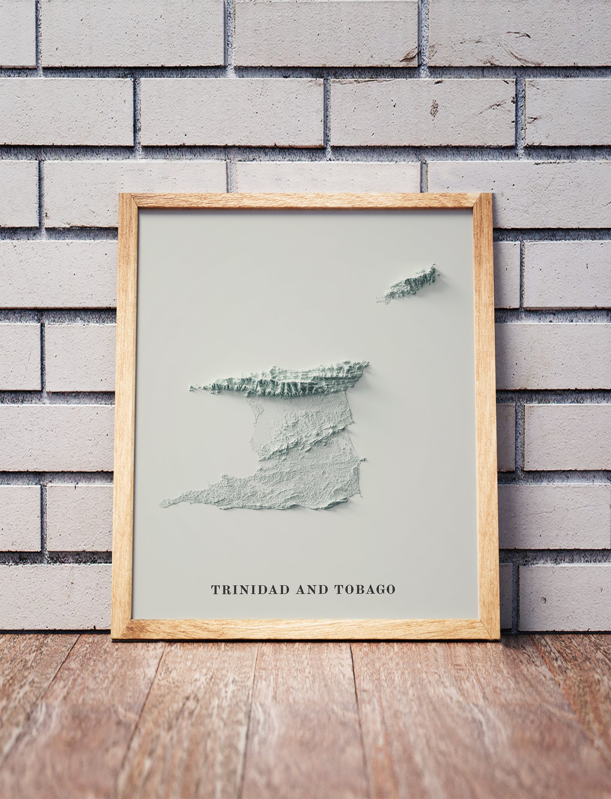 Trinidad and Tobago shaded relief map in a wooden frame. Realistic terrain art print for home decor, displayed against a brick wall