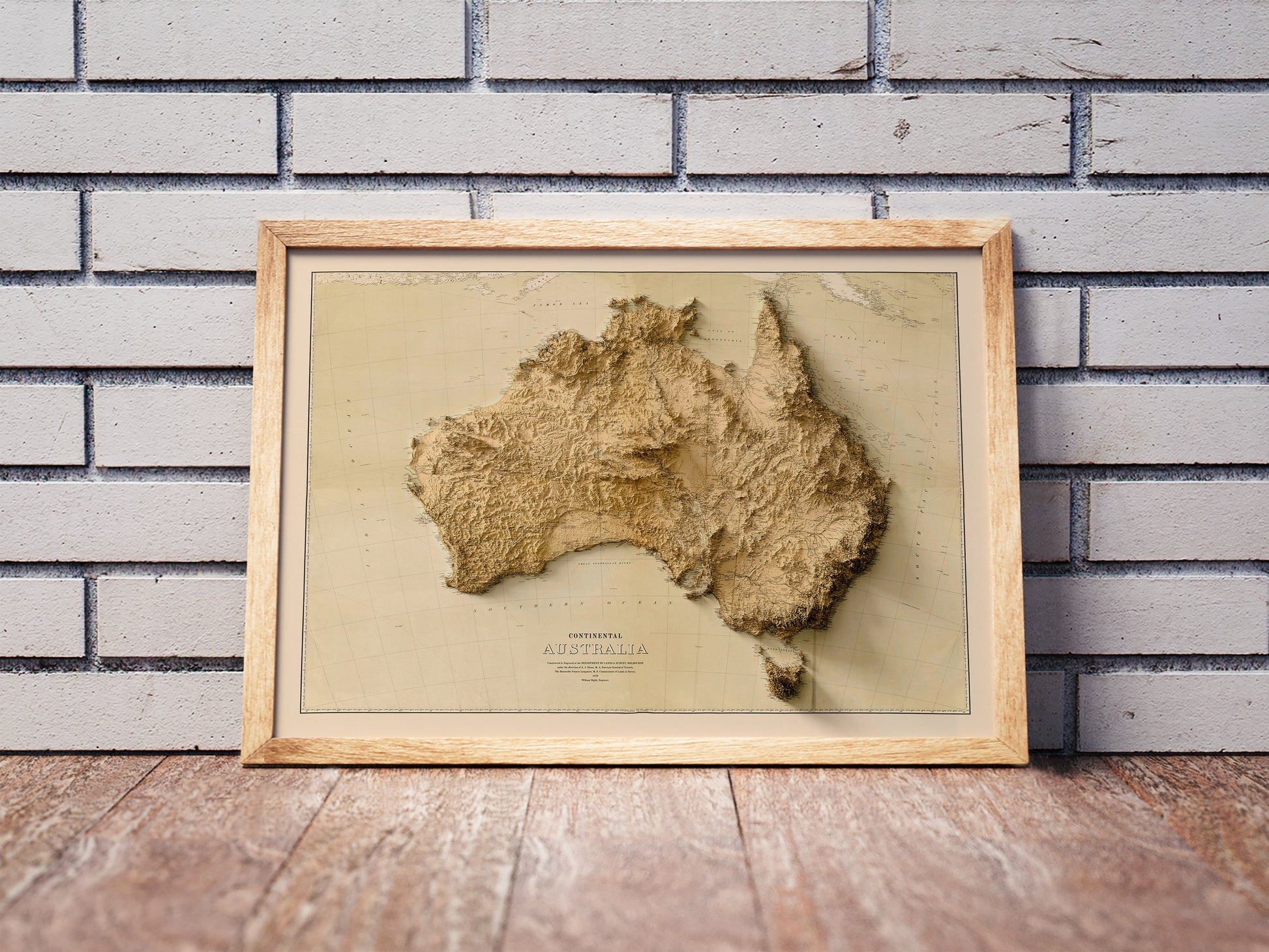 Vintage Australia shaded relief map in a wooden frame. Realistic terrain art print for home decor, displayed against a brick wall
