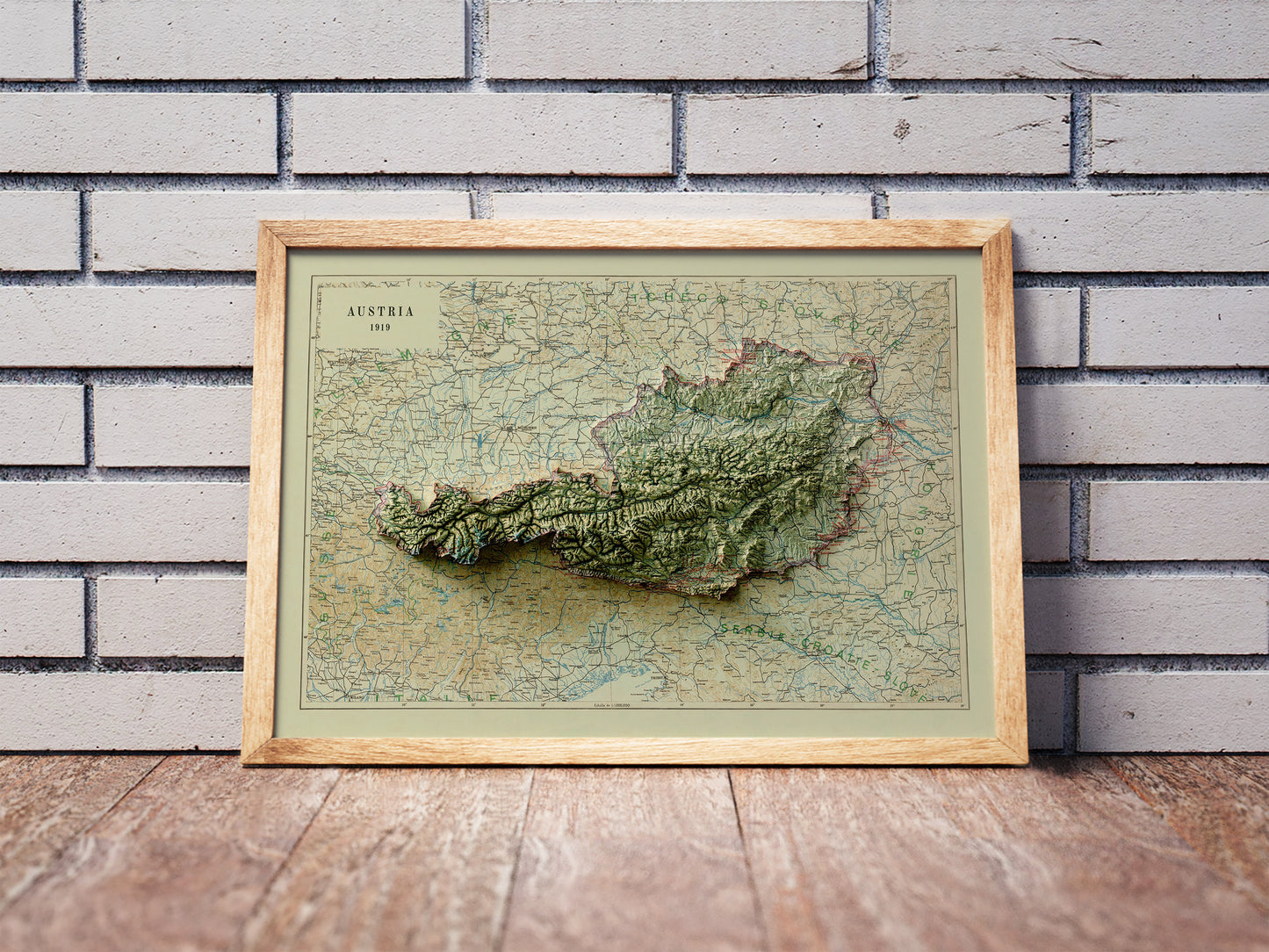 Vintage Austria shaded relief map in a wooden frame. Realistic terrain art print for home decor, displayed against a brick wall