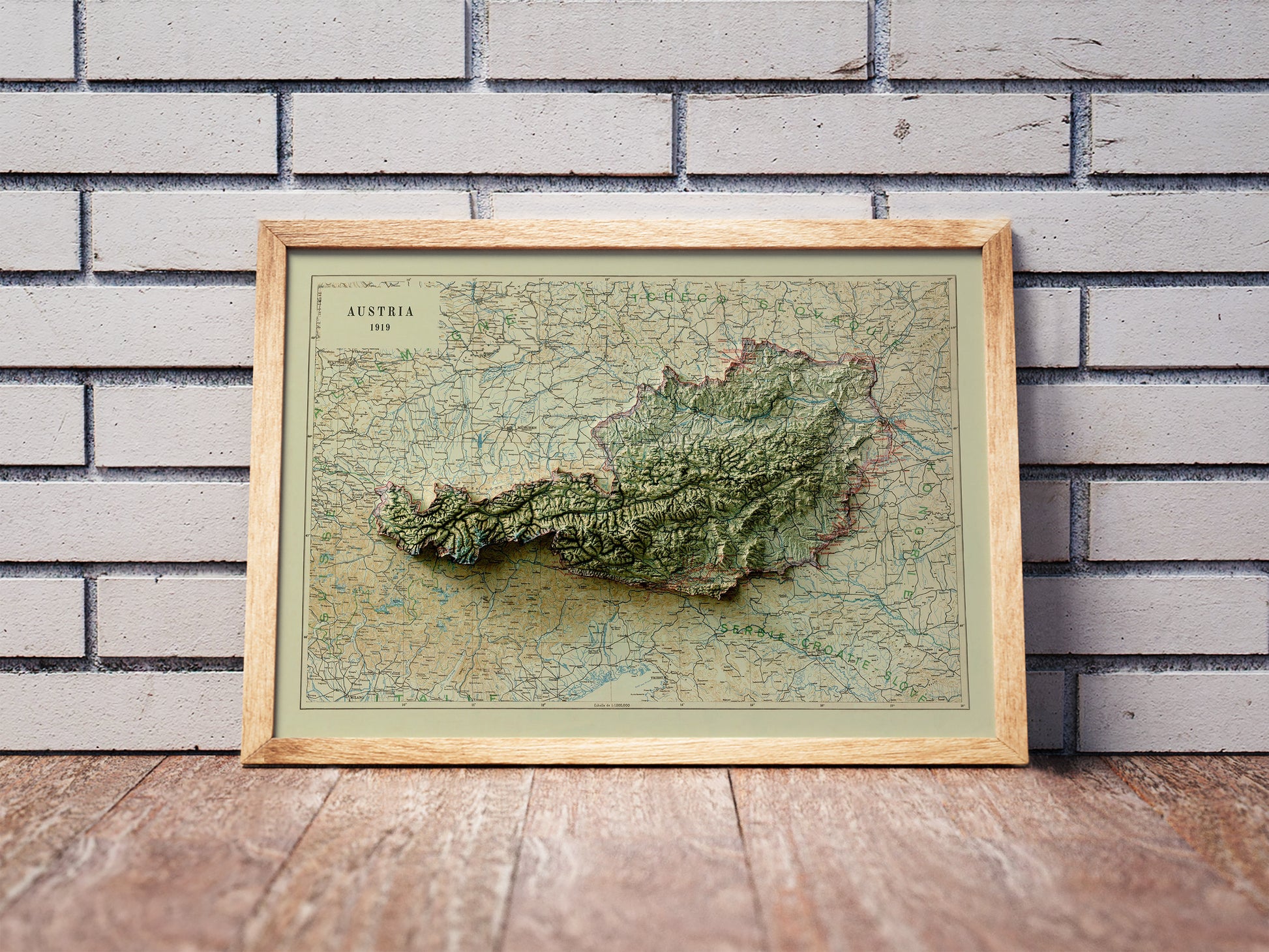 Vintage Austria shaded relief map in a wooden frame. Realistic terrain art print for home decor, displayed against a brick wall
