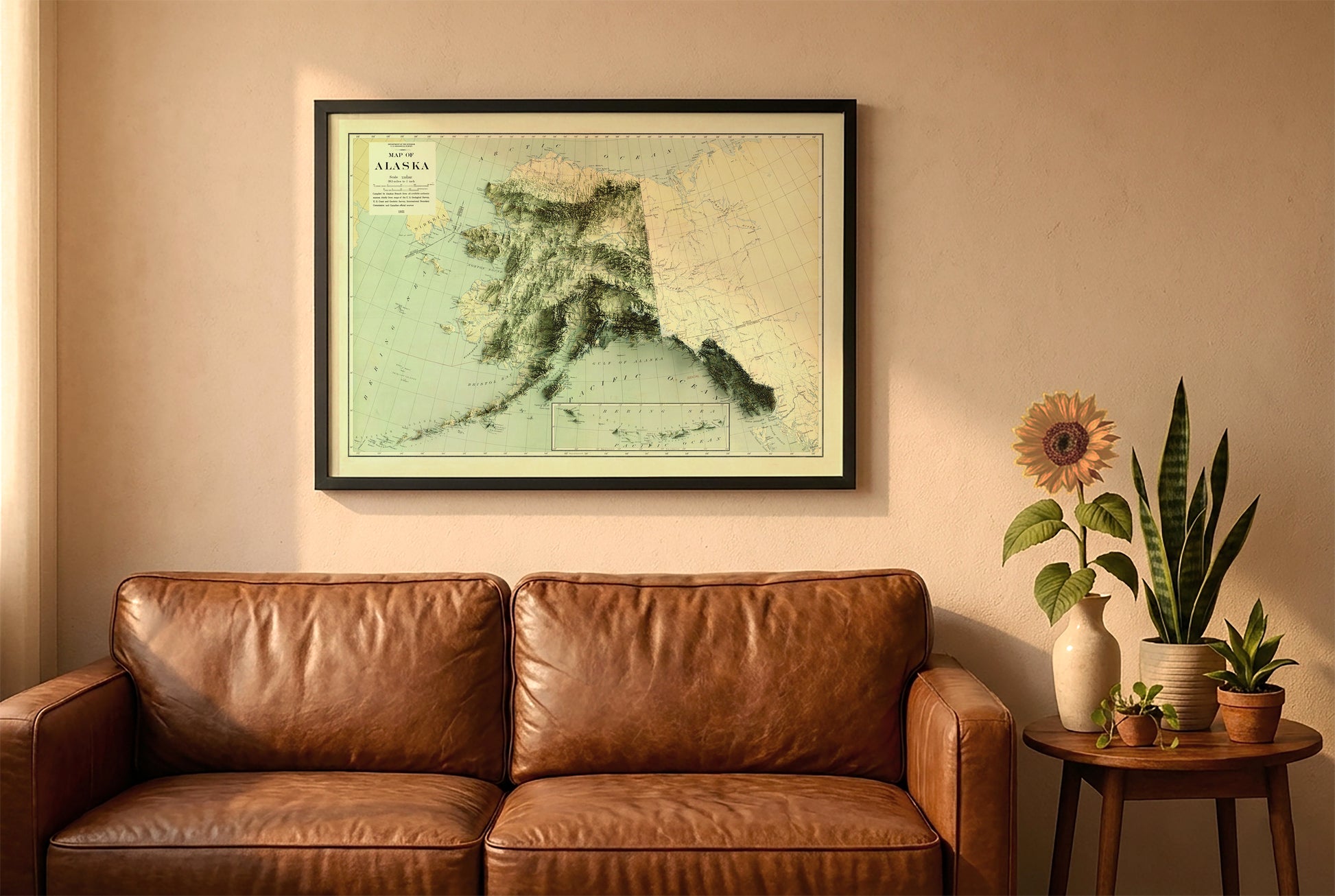 Alaska vintage relief map in a black frame above a brown leather sofa. Boho living room with warm sunlight, sunflower, and indoor plants on a wooden side table
