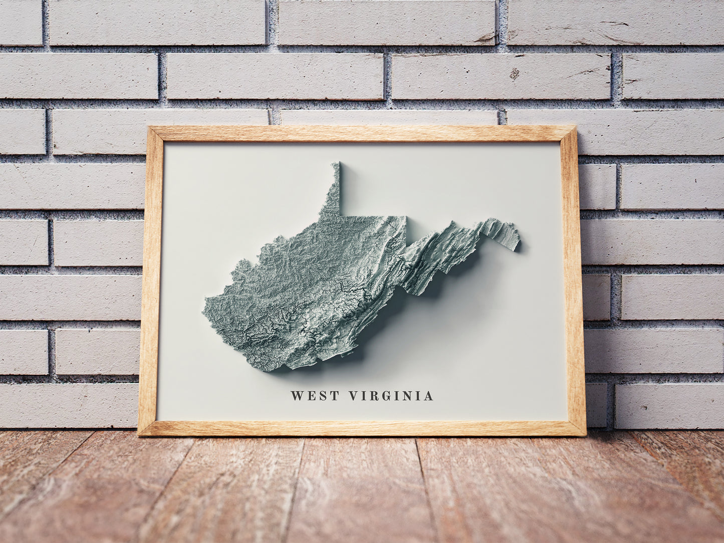 West Virginia shaded relief map in a wooden frame. Realistic terrain art print for home decor, displayed against a brick wall