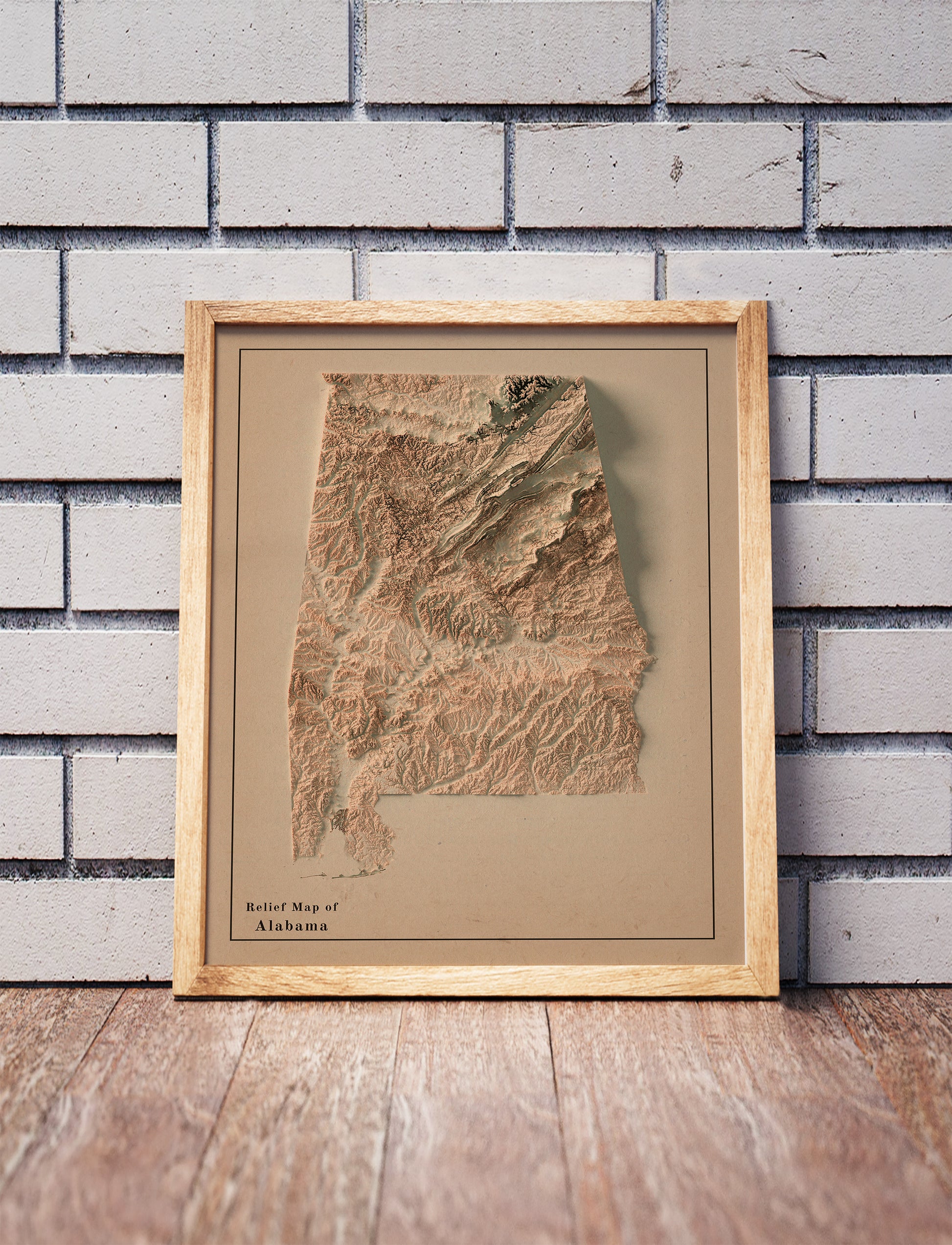 Vintage Alabama shaded relief map in a wooden frame. Realistic terrain art print for home decor, displayed against a brick wall