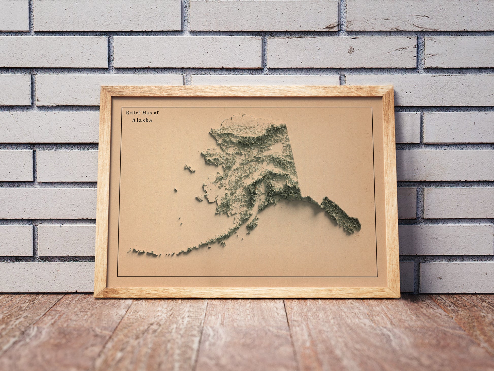 Vintage Alaska shaded relief map in a wooden frame. Realistic terrain art print for home decor, displayed against a brick wall