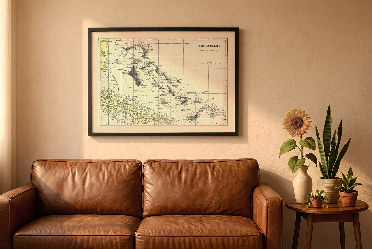 Bahamas vintage relief map in a black frame above a brown leather sofa. Boho living room with warm sunlight, sunflower, and indoor plants on a wooden side table