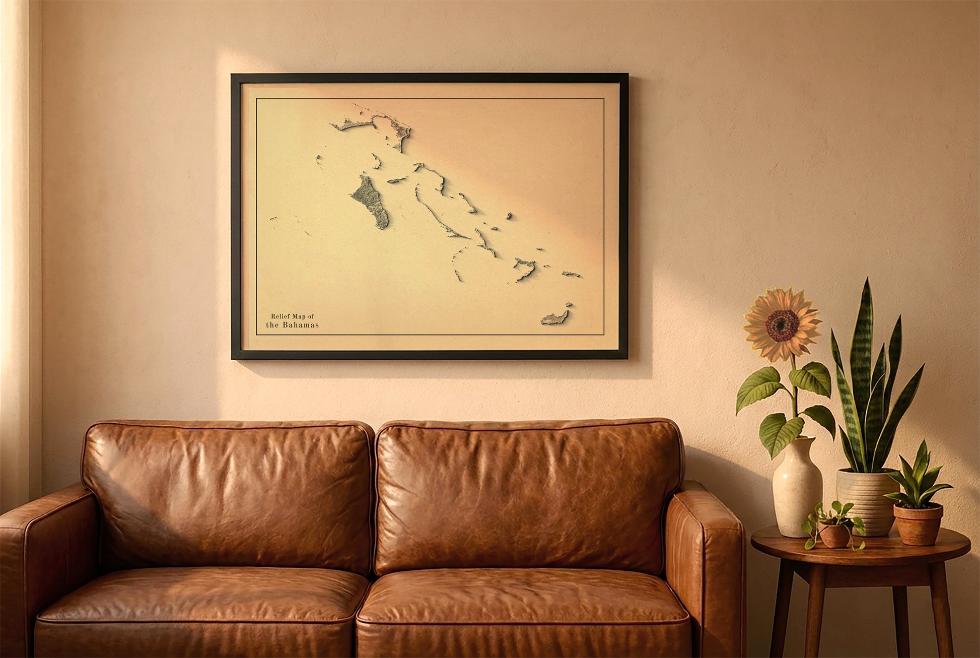 Bahamas vintage relief map in a black frame above a brown leather sofa. Boho living room with warm sunlight, sunflower, and indoor plants on a wooden side table