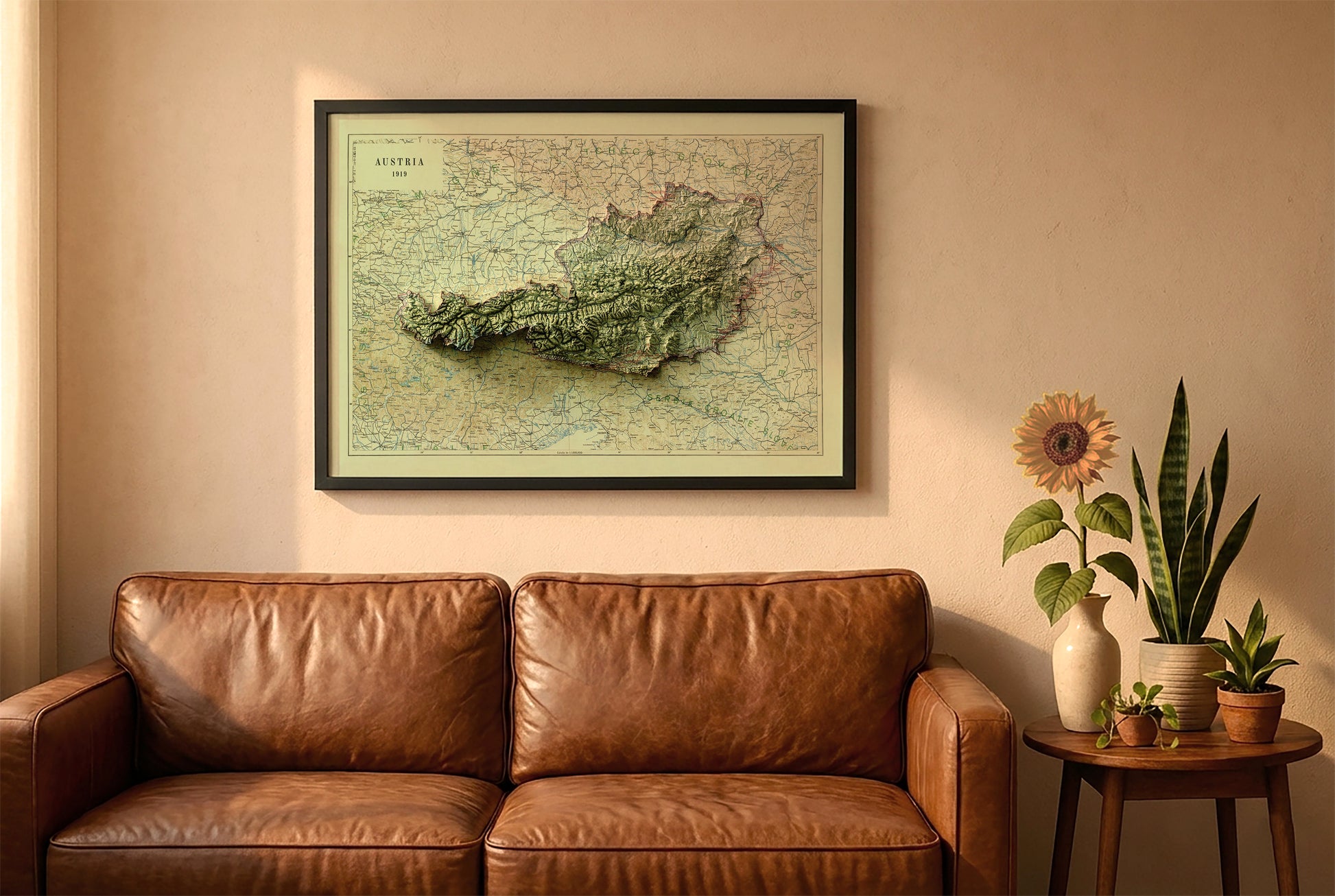 Austria vintage relief map in a black frame above a brown leather sofa. Boho living room with warm sunlight, sunflower, and indoor plants on a wooden side table