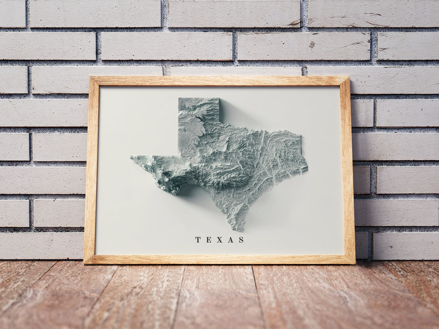 Texas shaded relief map in a wooden frame. Realistic terrain art print for home decor, displayed against a brick wall
