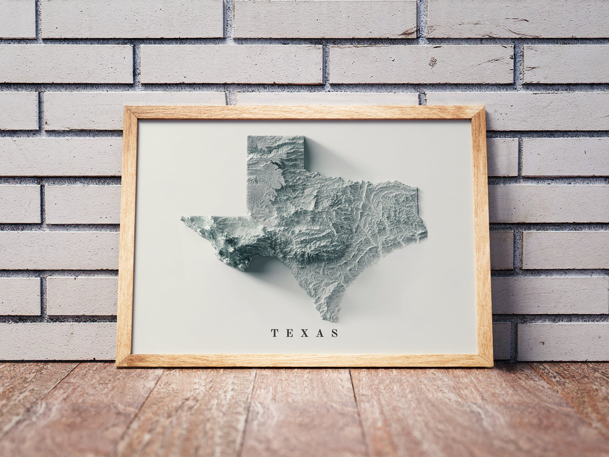 Texas shaded relief map in a wooden frame. Realistic terrain art print for home decor, displayed against a brick wall