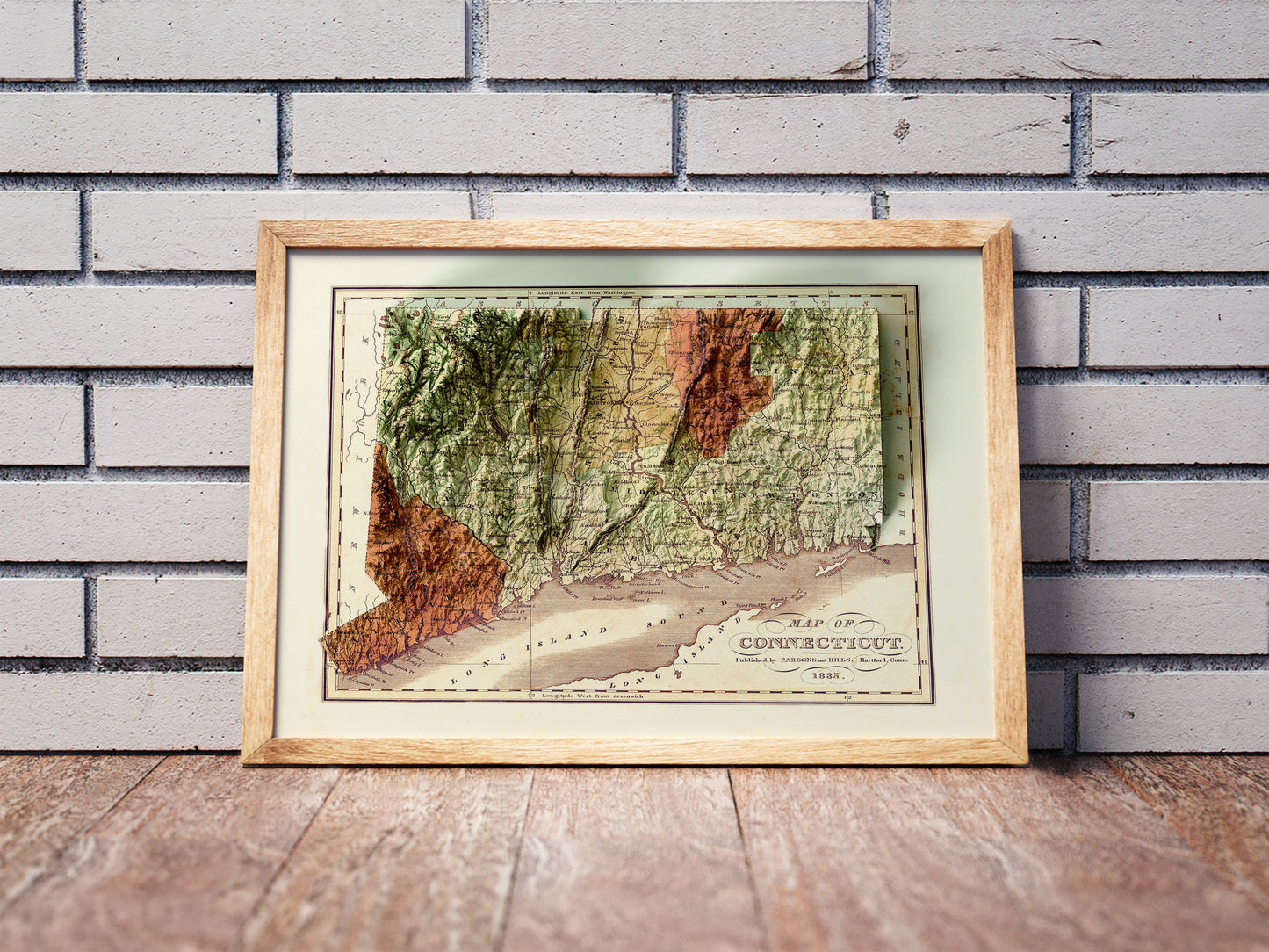 Vintage Connecticut shaded relief map in a wooden frame. Realistic terrain art print for home decor, displayed against a brick wall