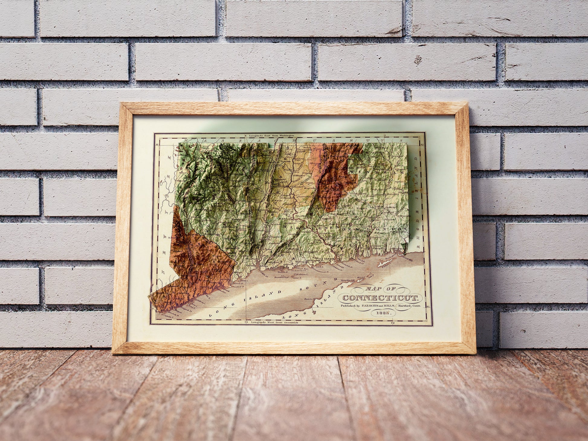 Vintage Connecticut shaded relief map in a wooden frame. Realistic terrain art print for home decor, displayed against a brick wall