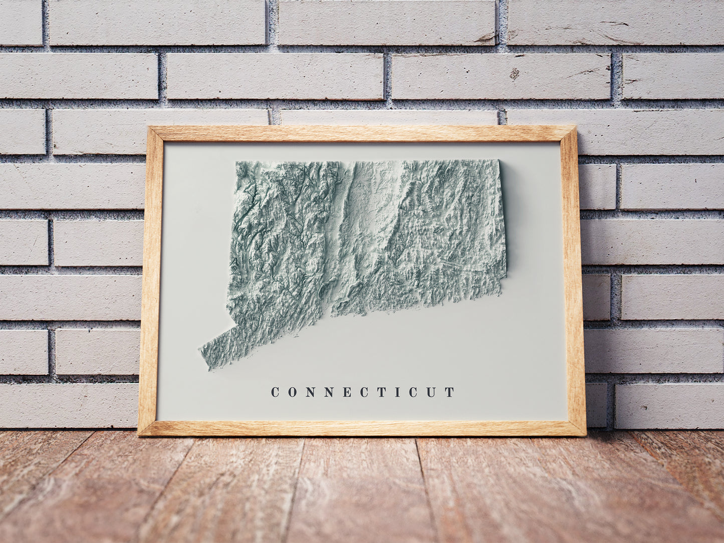 Connecticut shaded relief map in a wooden frame. Realistic terrain art print for home decor, displayed against a brick wall