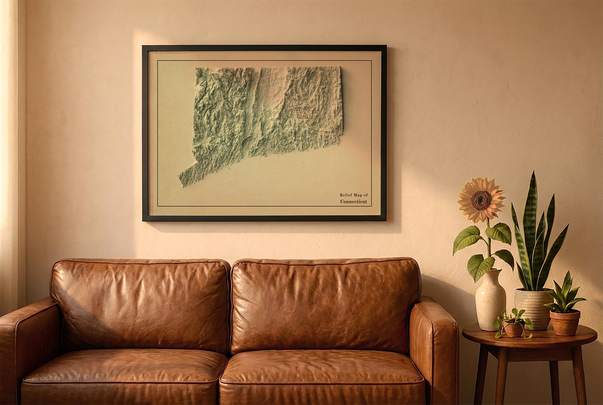 Connecticut vintage relief map in a black frame above a brown leather sofa. Boho living room with warm sunlight, sunflower, and indoor plants on a wooden side table