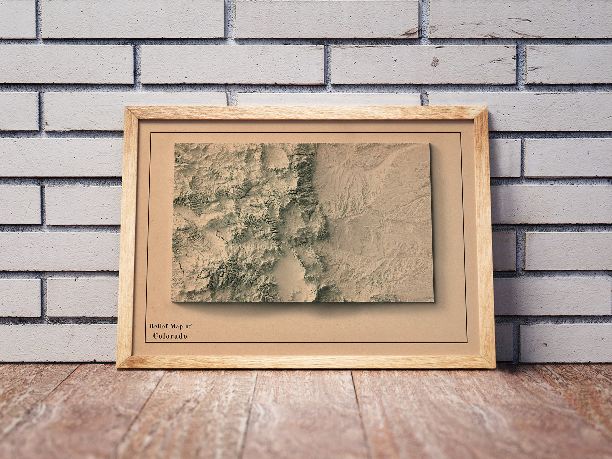 Vintage Colorado shaded relief map in a wooden frame. Realistic terrain art print for home decor, displayed against a brick wall