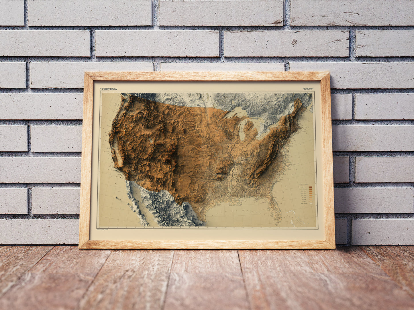 Vintage United States shaded relief map in a wooden frame. Realistic terrain art print for home decor, displayed against a brick wall