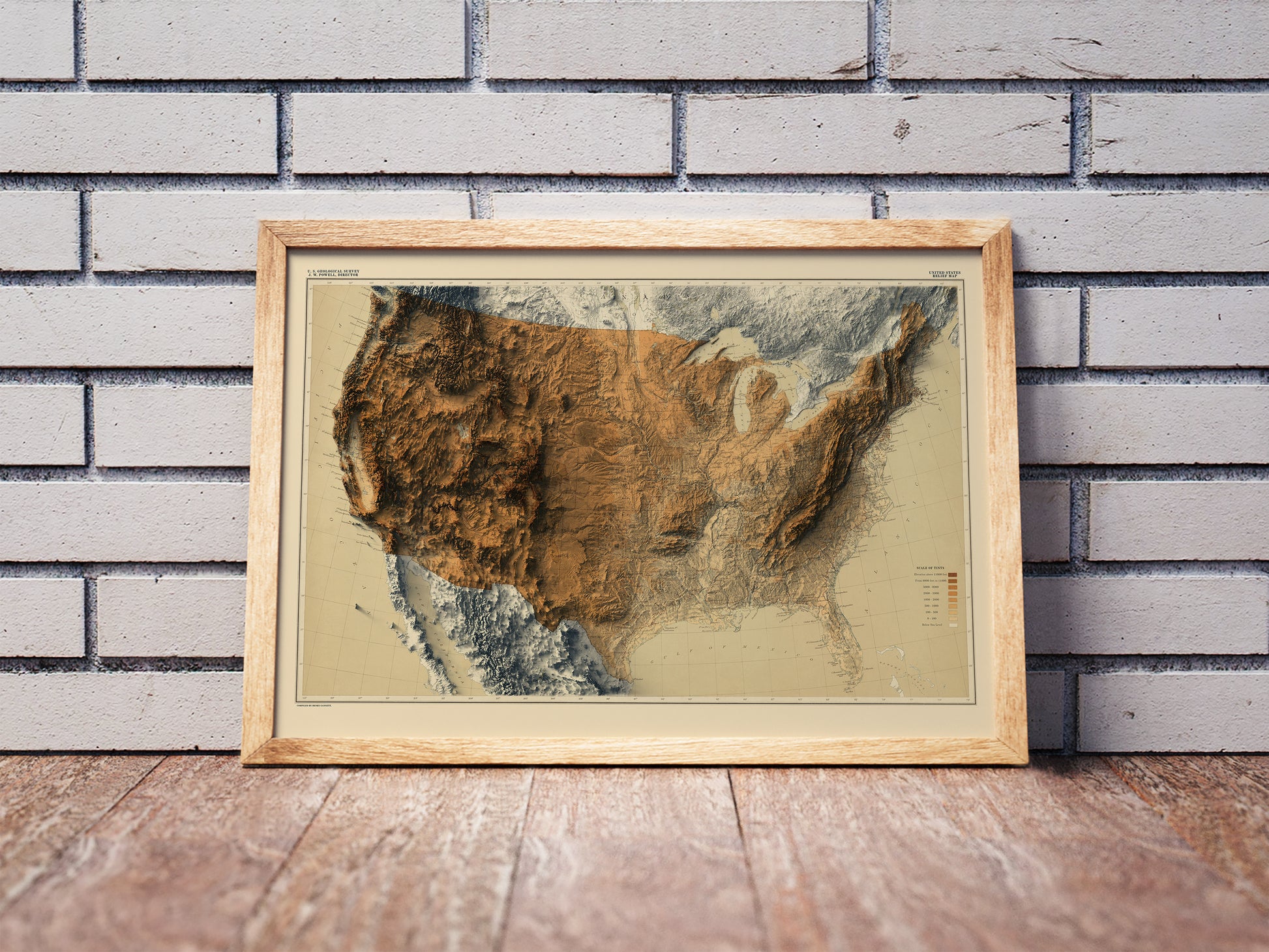 Vintage United States shaded relief map in a wooden frame. Realistic terrain art print for home decor, displayed against a brick wall