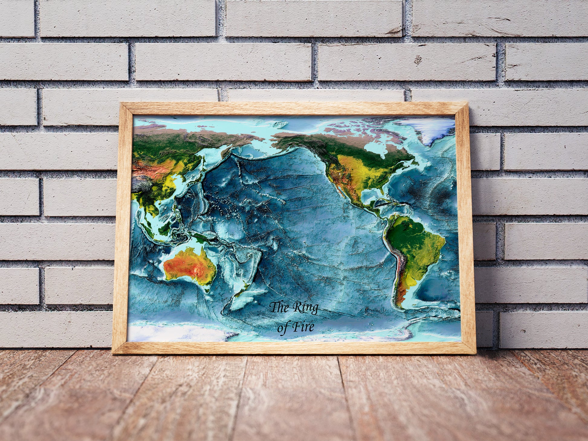 Ring of Fire shaded relief map in a wooden frame. Realistic terrain art print for home decor, displayed against a brick wall
