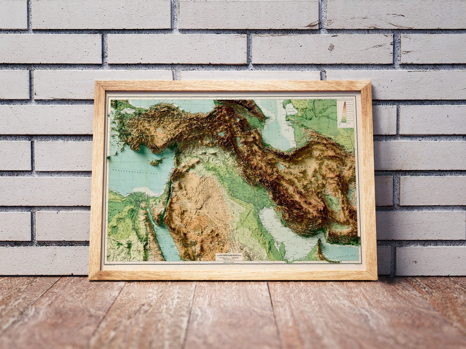 Vintage West Asia shaded relief map in a wooden frame. Realistic terrain art print for home decor, displayed against a brick wall
