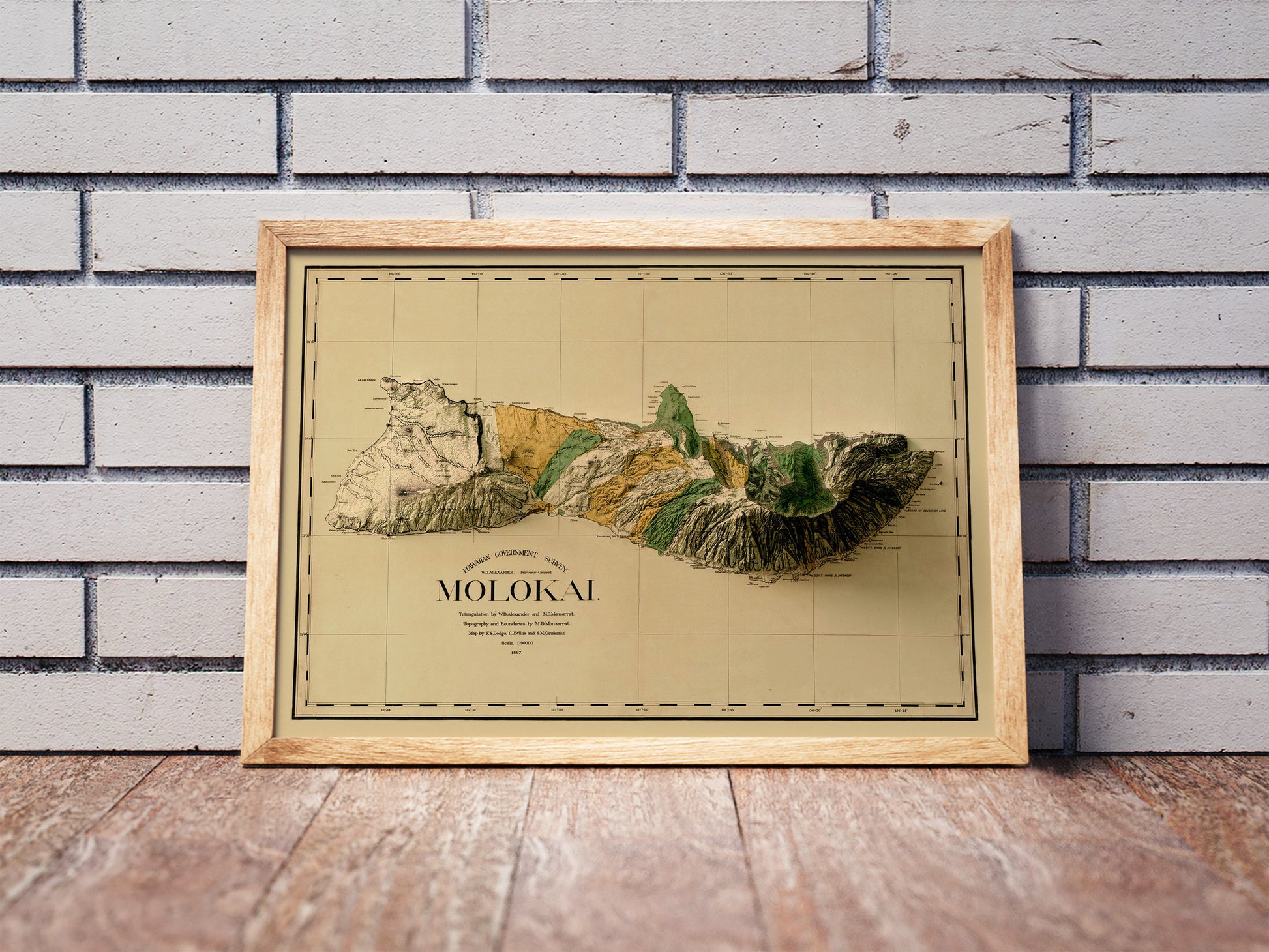 Vintage Molokai, Hawaii, shaded relief map in a wooden frame. Realistic terrain art print for home decor, displayed against a brick wall
